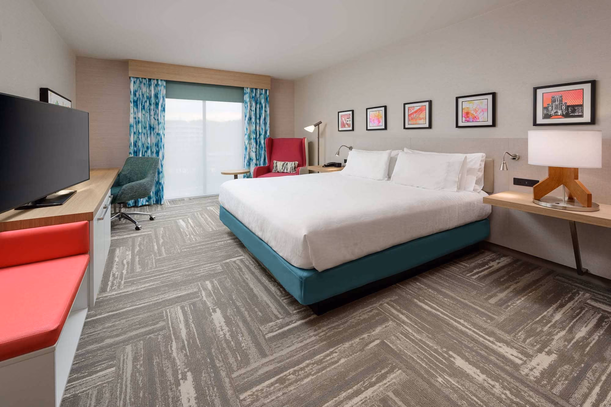 Modern hotel room with king bed, desk, TV, and colorful chairs