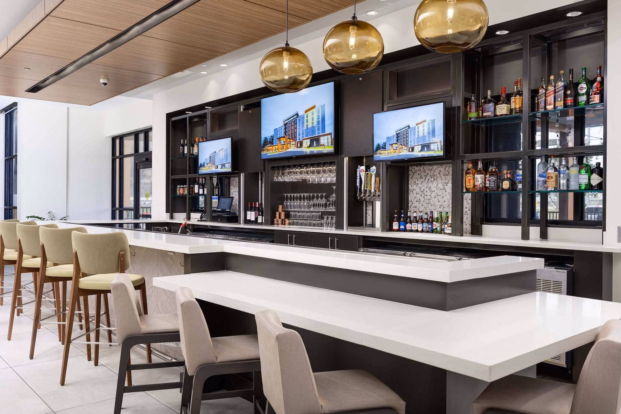 Modern hotel bar with white counters, pendant lights, and wall-mounted TVs, D&S Builders hospitality construction