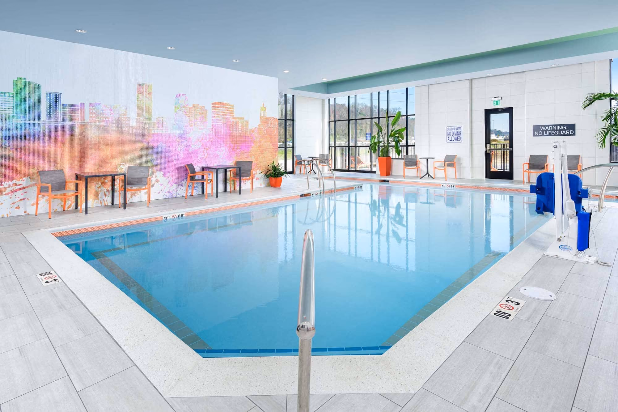 Indoor hotel pool with colorful mural, seating, and large windows