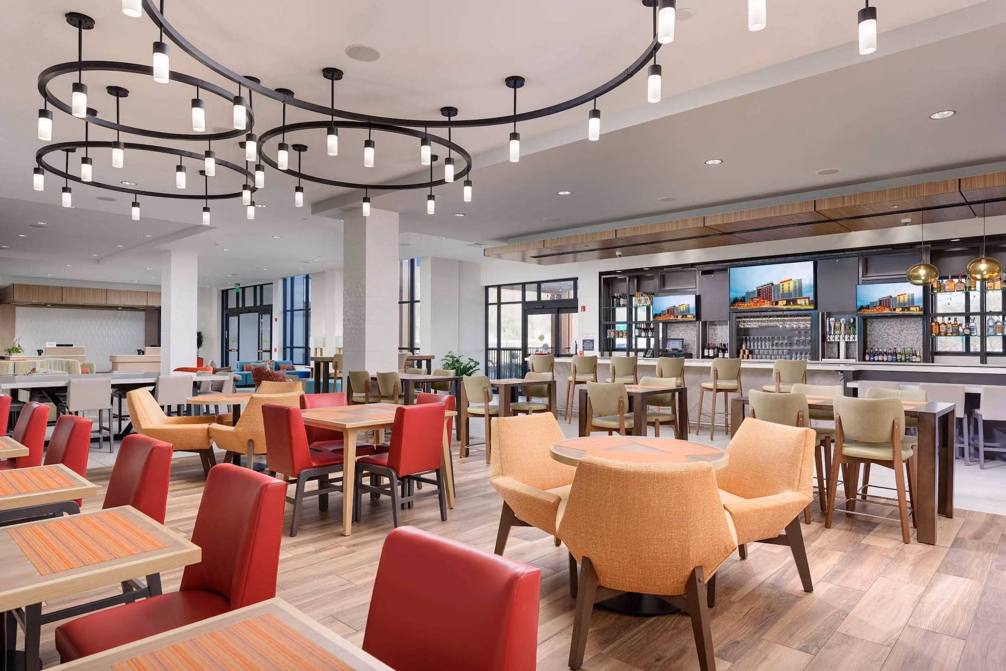 Modern hotel dining area with colorful chairs, tables, and a bar under circular ceiling lights.
