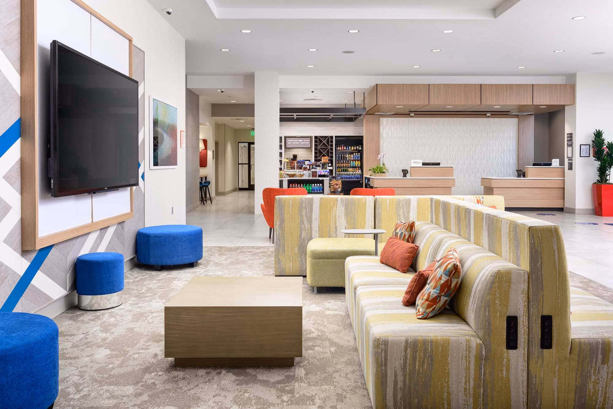 Modern hotel lobby seating area with reception desks and a large wall-mounted TV