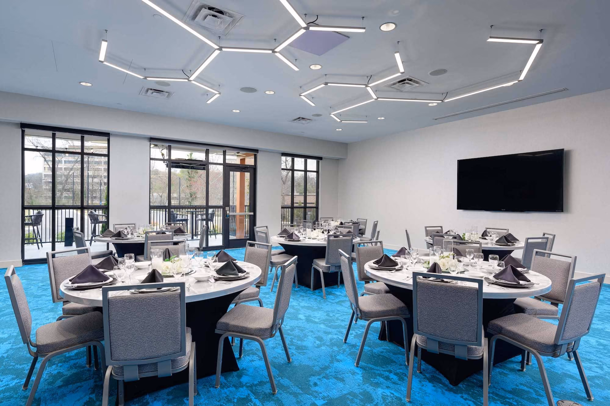 Modern hospitality dining room with round tables, blue carpet, and geometric ceiling lights