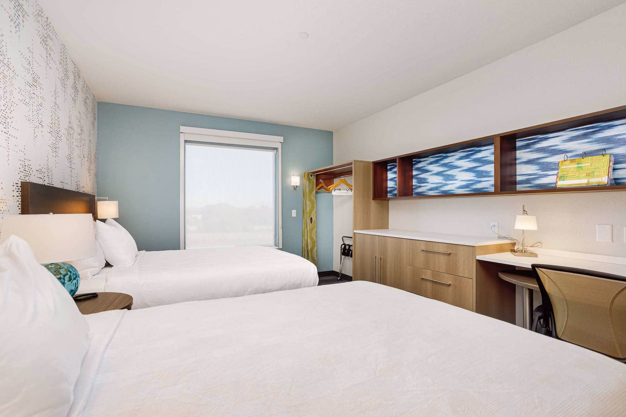Modern hotel room with two beds, desk, and built-in storage by D&S Builders