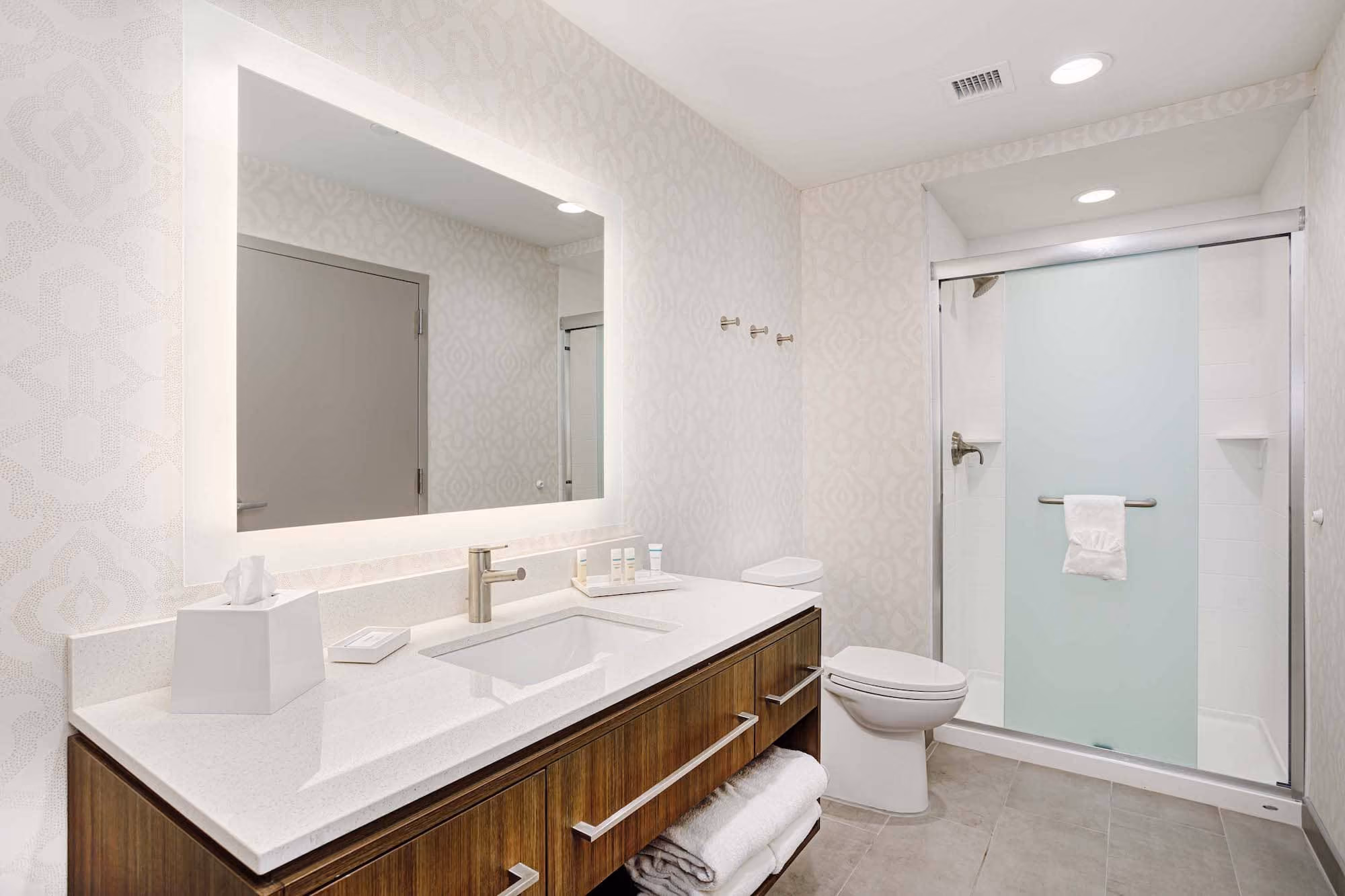 Modern bathroom with vanity, large mirror, toilet, and frosted glass shower door by D&S Builders