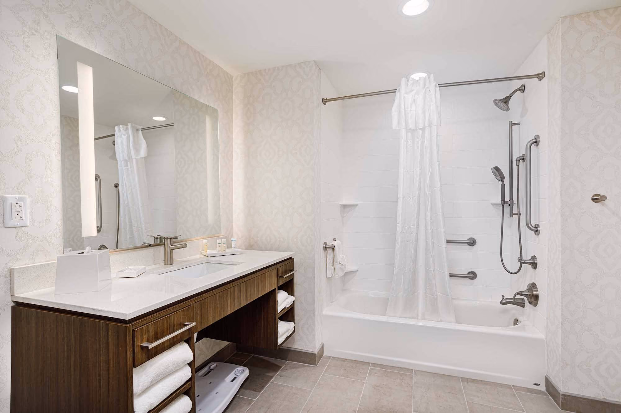 Accessible hotel bathroom with vanity, large mirror, and walk-in tub shower, by D&S Builders