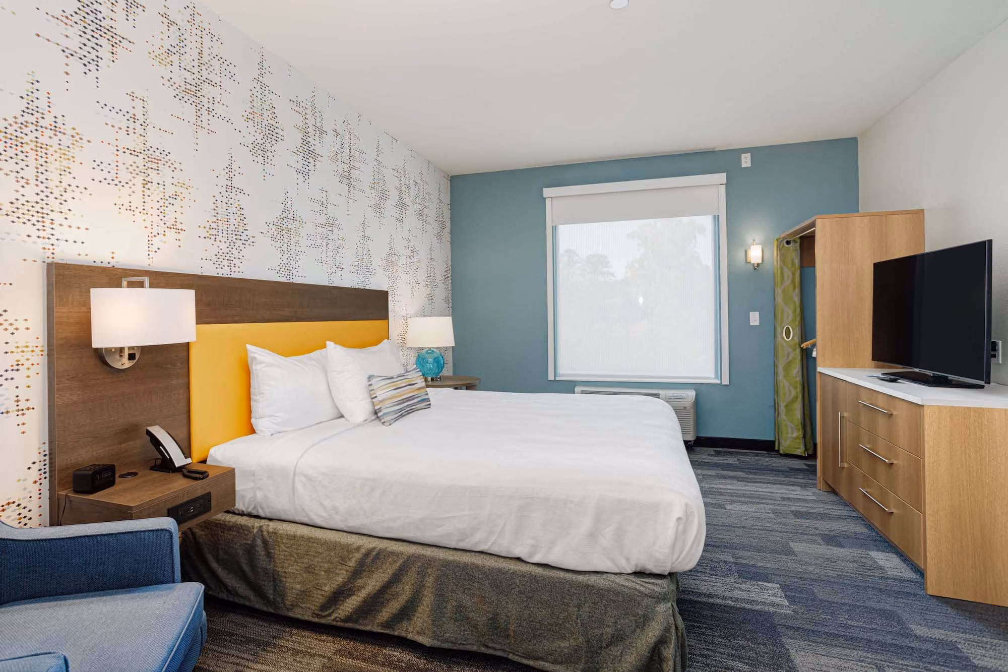 Modern hotel room with a bed, TV, and blue accent wall, likely hospitality construction by D&S Builders