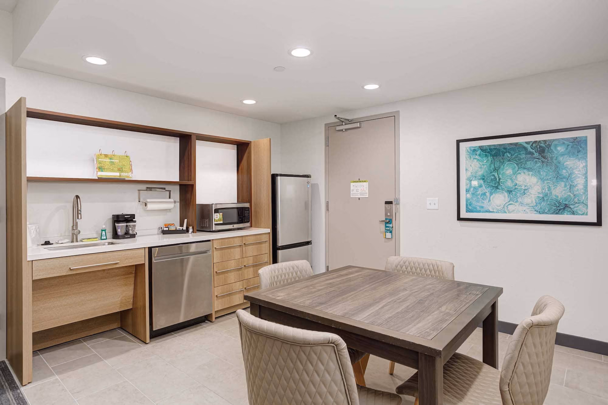 Modern hospitality kitchenette and dining area with table, chairs, sink, fridge, and microwave