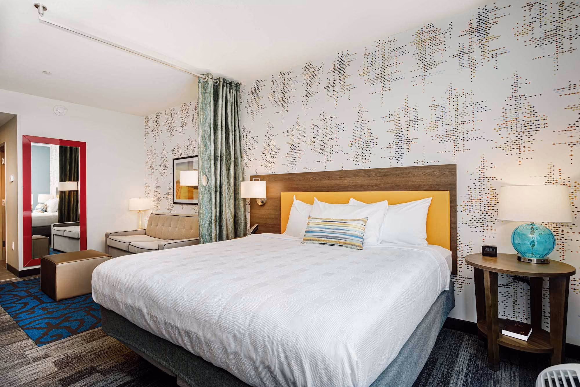 Modern hotel room with king bed, patterned accent wall, and seating area