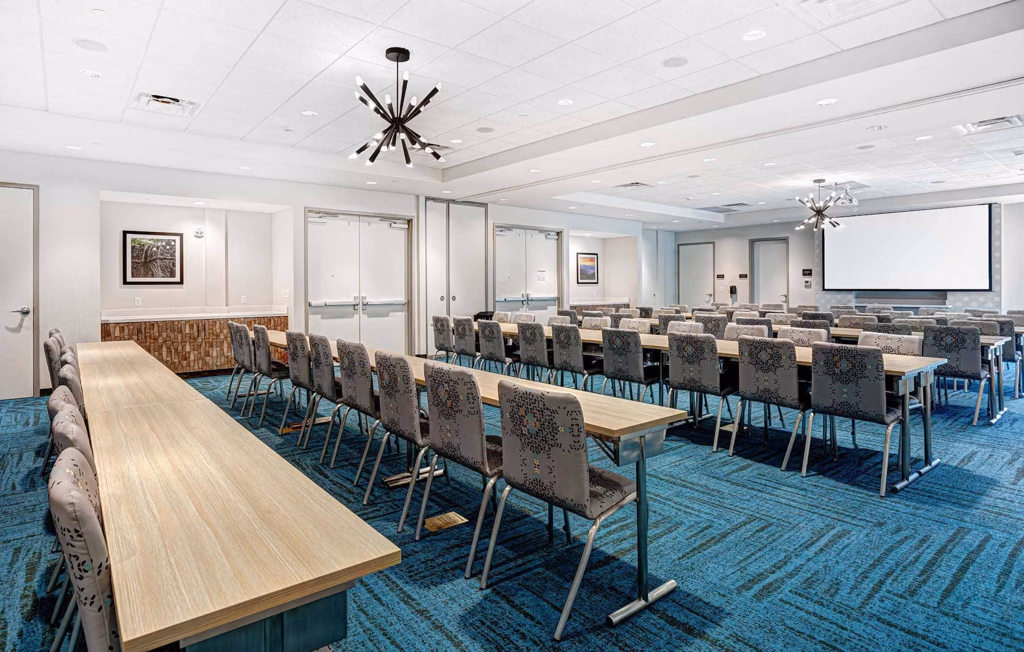 Modern hotel meeting room with rows of chairs, tables, and a projection screen