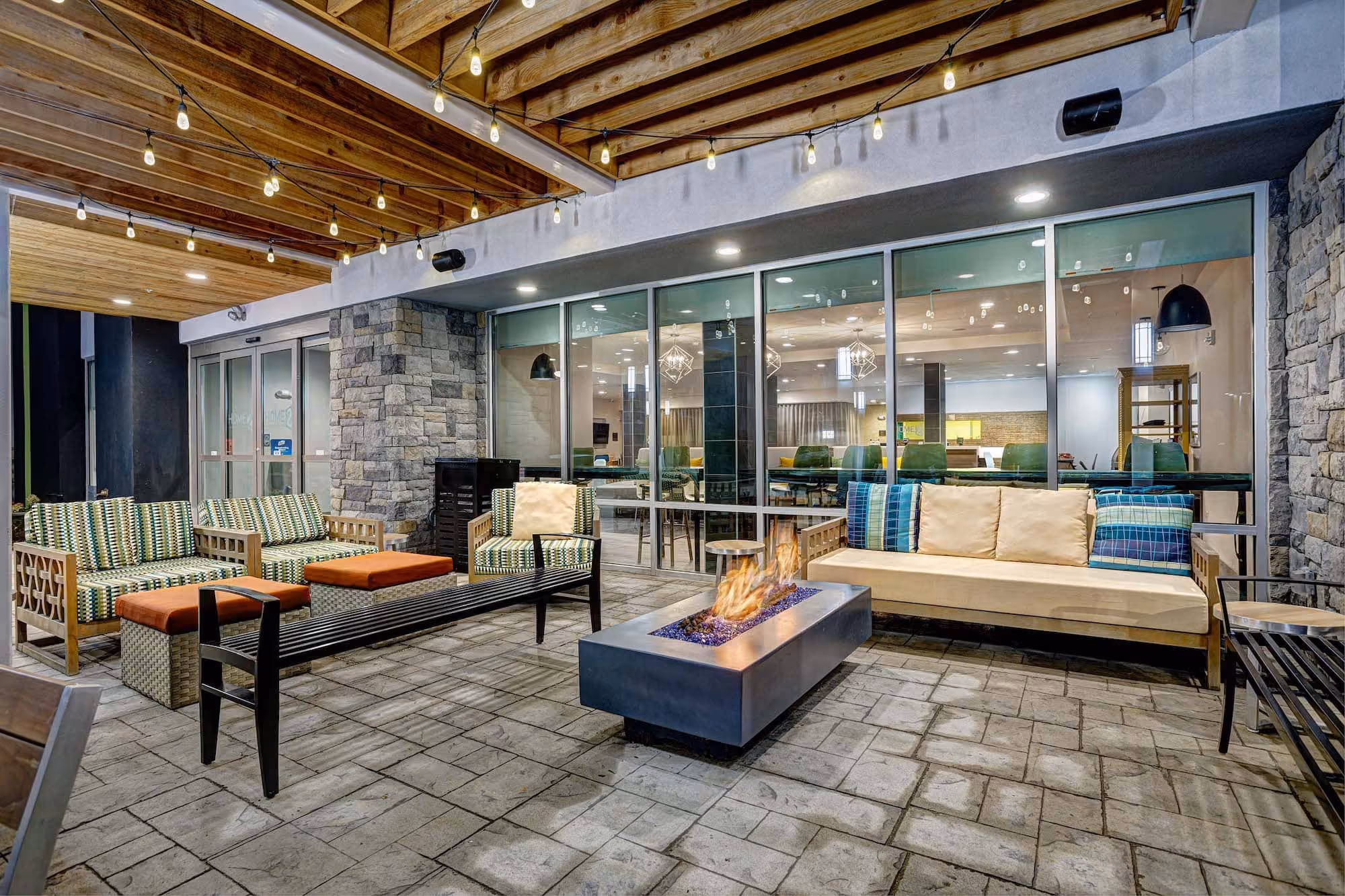 Covered outdoor hospitality seating area with fire pit and string lights