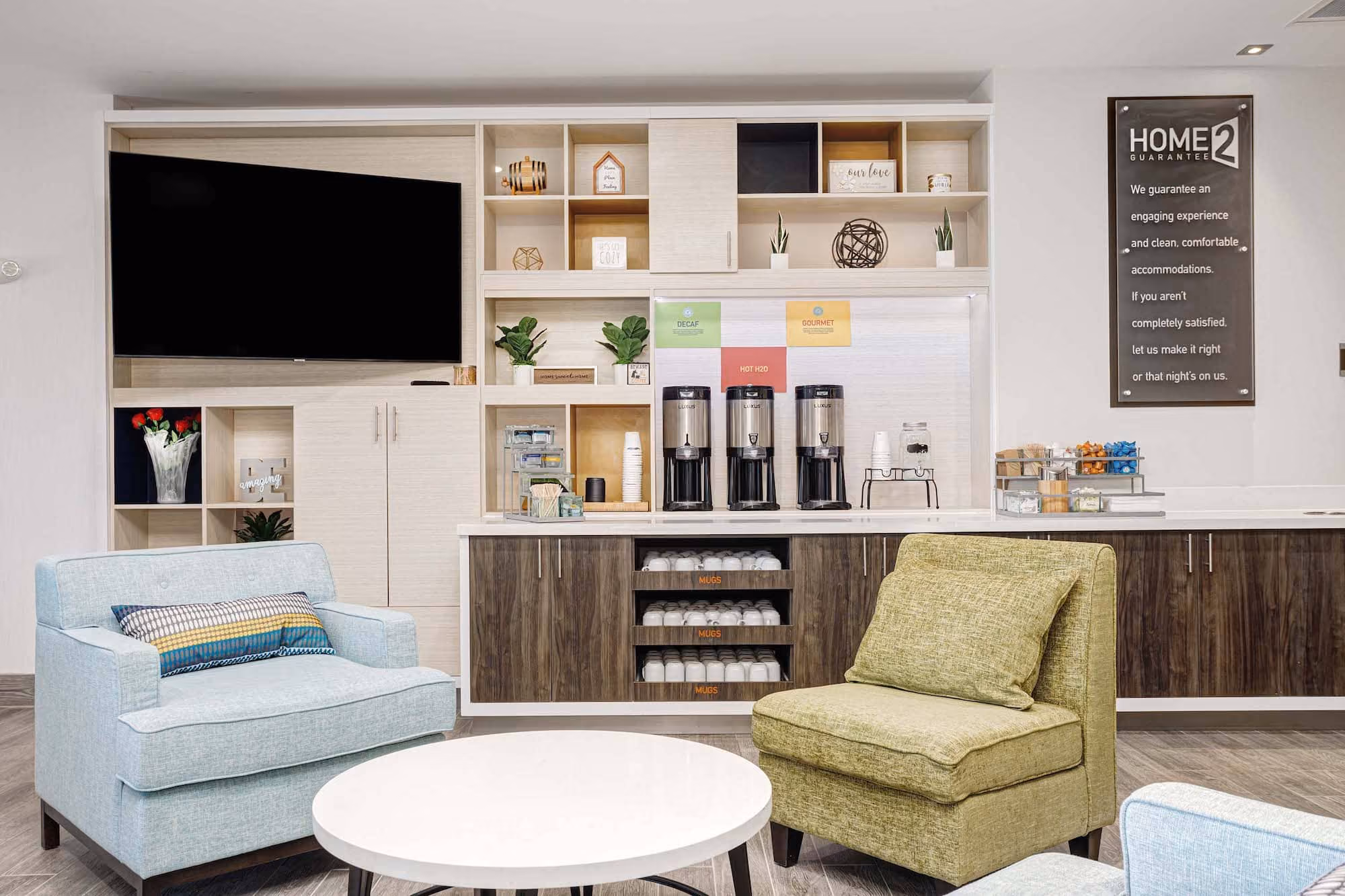 Hotel lounge with coffee station, TV, and colorful chairs by D&S Builders
