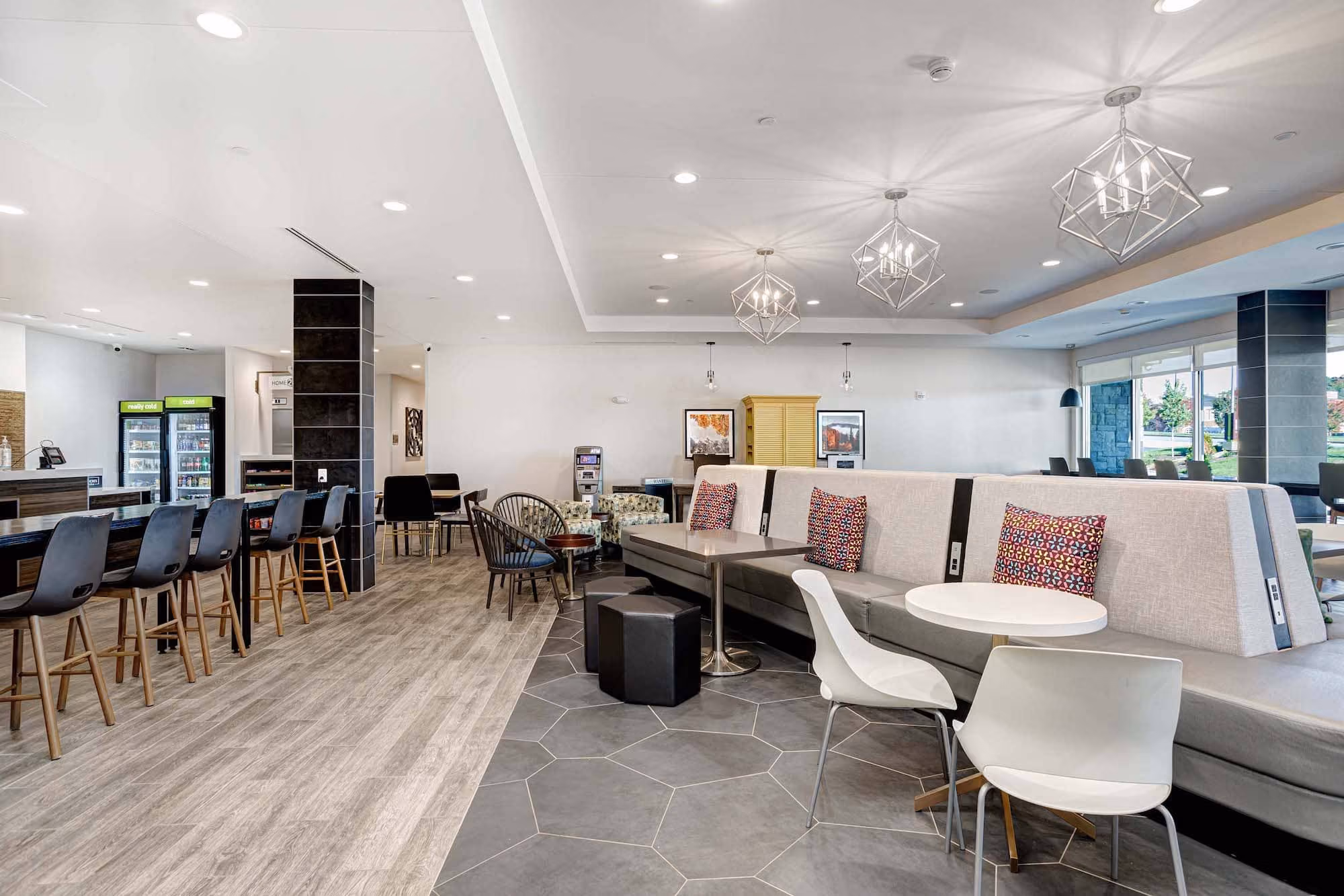 Modern hotel lobby seating area with bar stools, lounge booths, and geometric pendant lights.