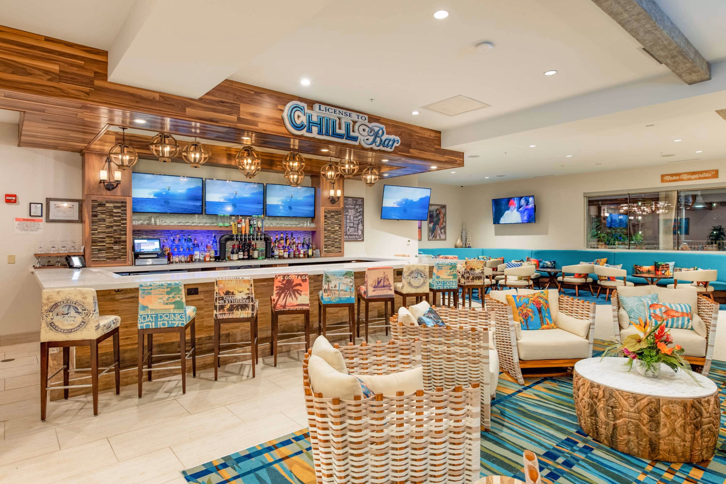 Modern hotel bar and lounge with colorful seating and wall-mounted TVs