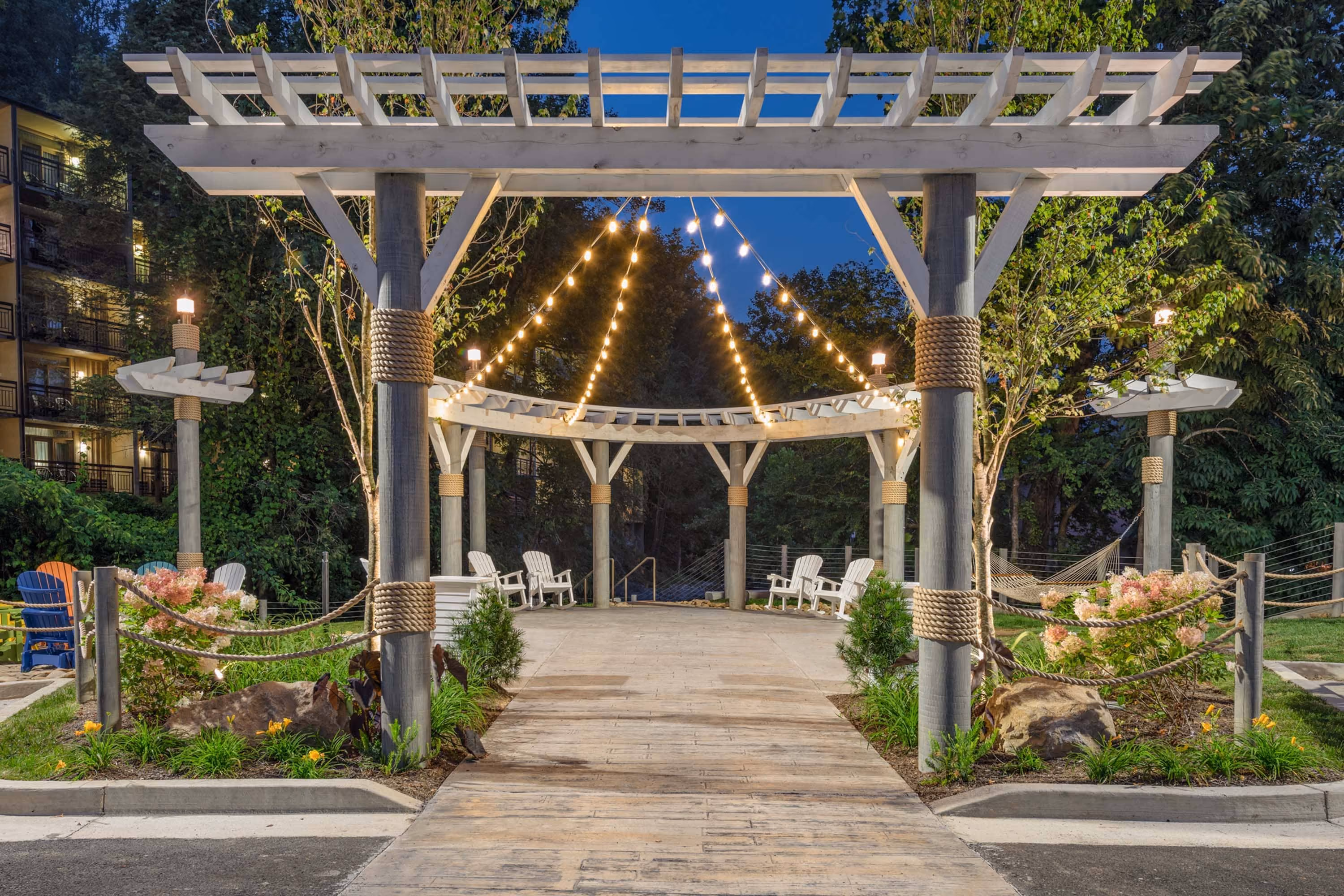 Lit pergola walkway with string lights and seating in a landscaped hospitality courtyard