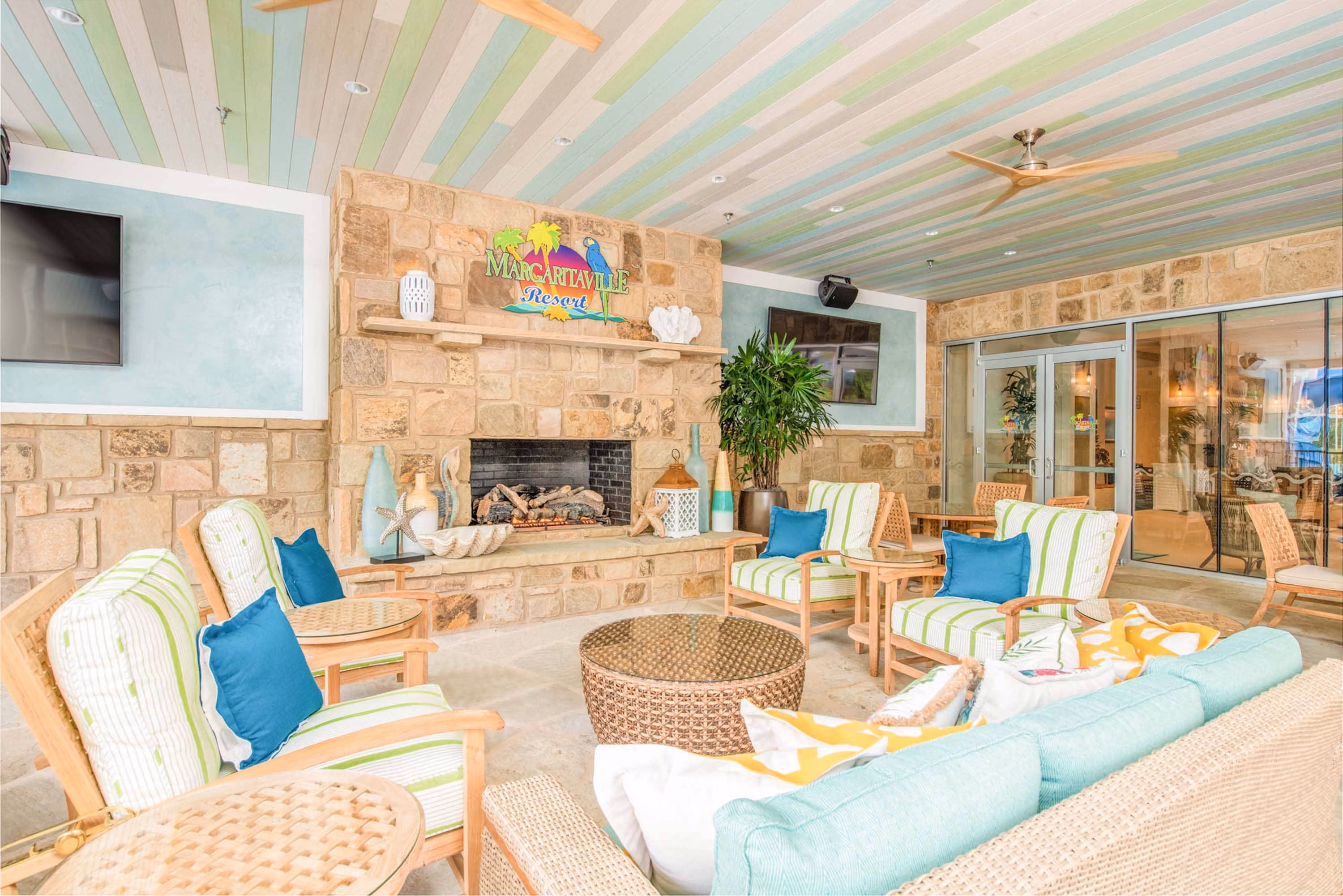 Resort lounge with stone fireplace, striped ceiling, and wicker seating by D&S Builders