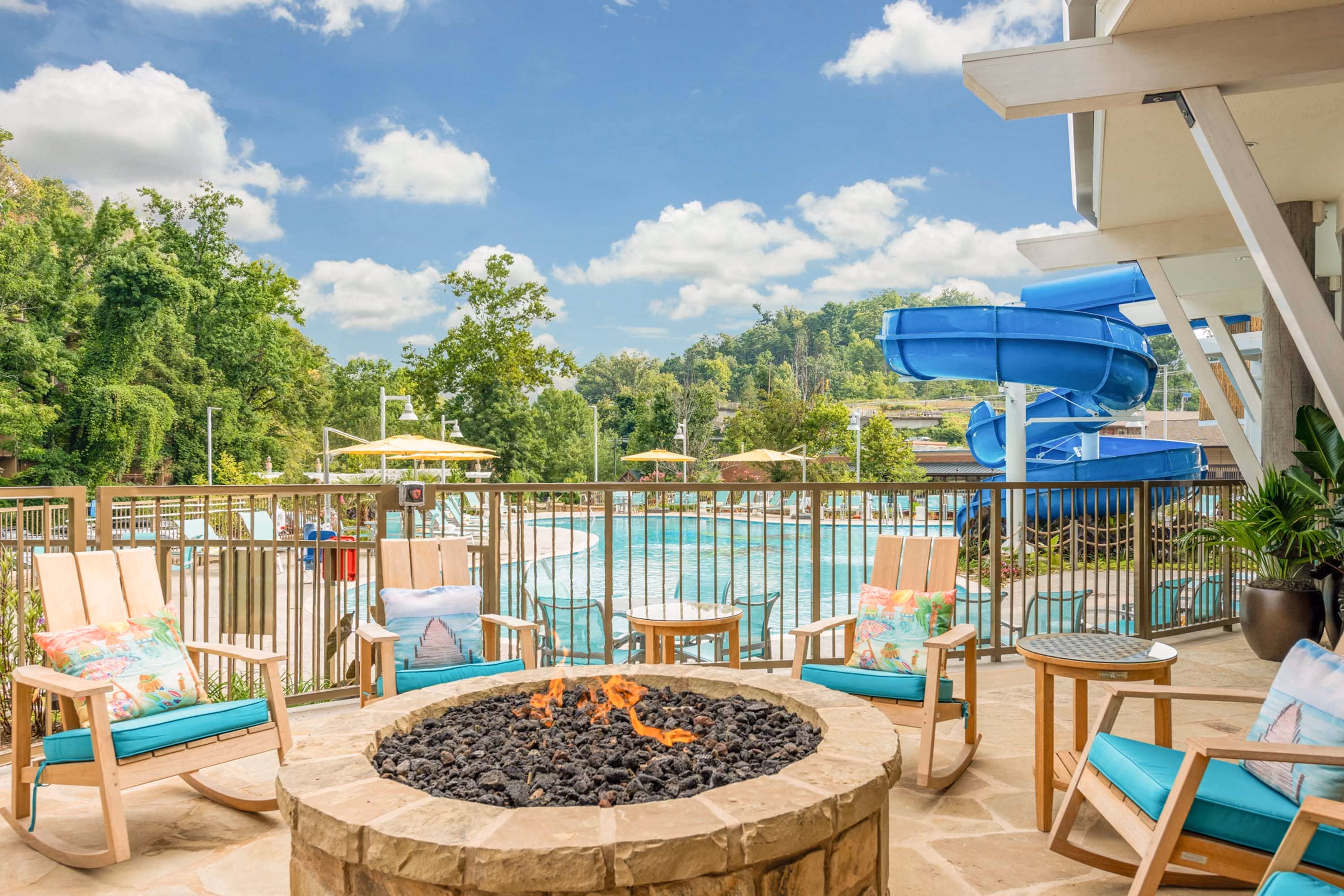 Resort pool deck with fire pit, rocking chairs, and a blue waterslide at D&S Builders