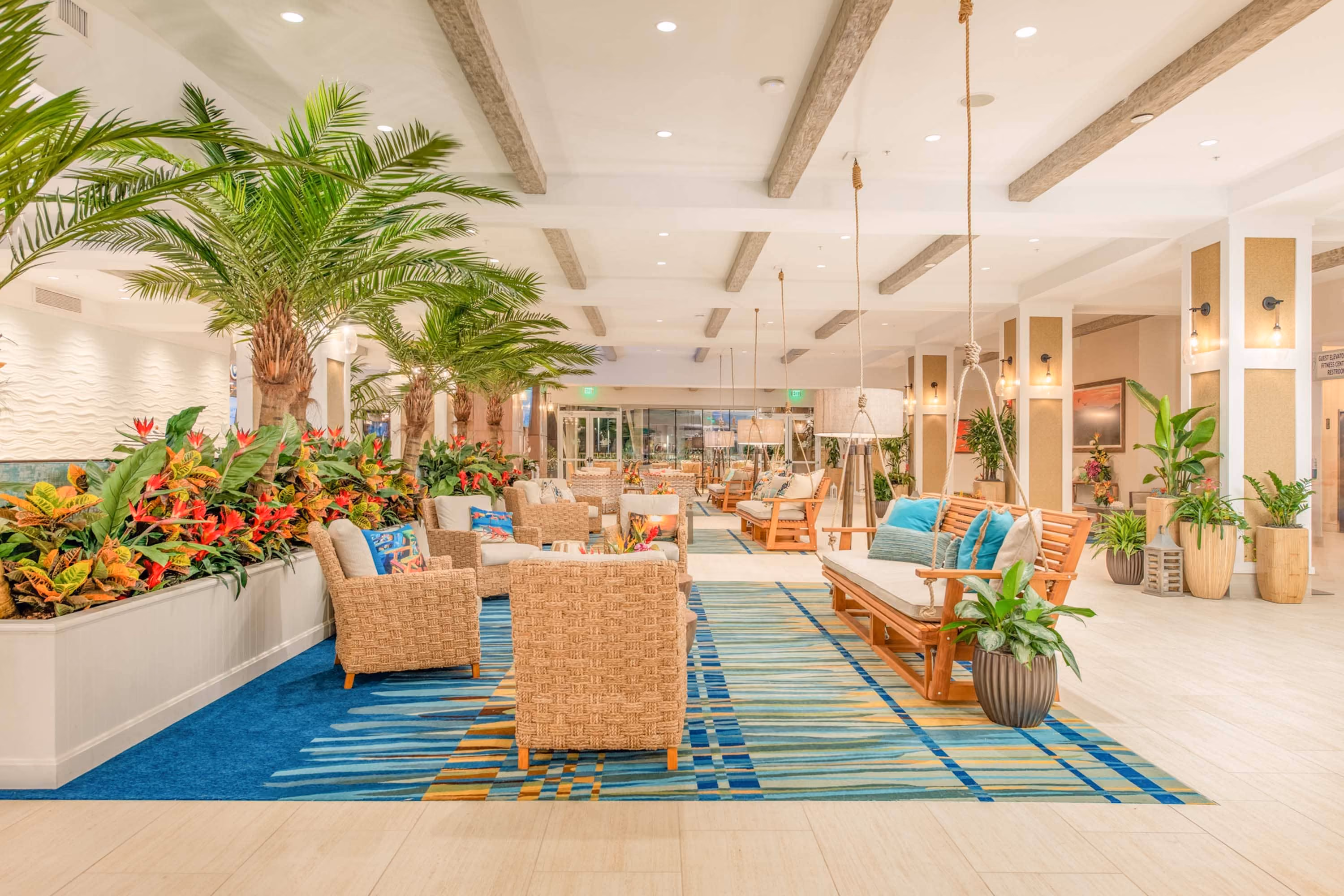 Bright tropical-style hotel lobby with wicker seating, hanging swings, and lush plants