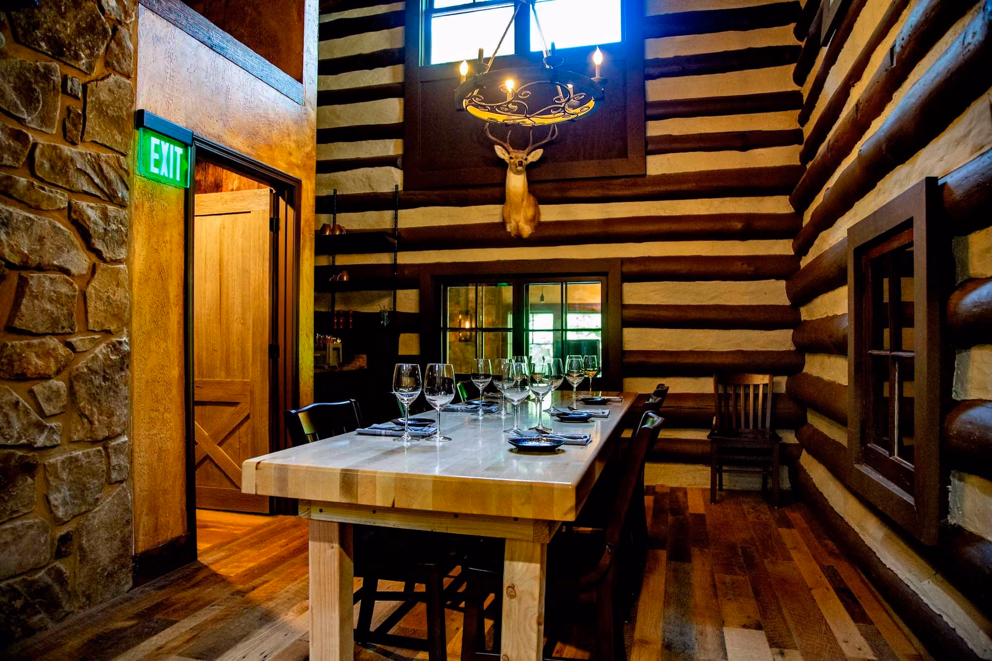 Rustic dining room with log walls, stone accents, and a long set table under a chandelier.