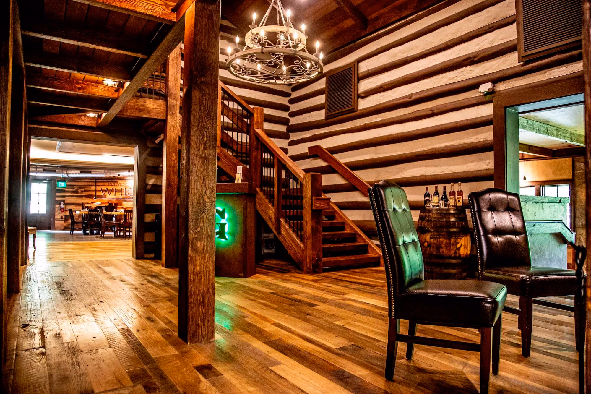 Rustic lodge-style hospitality interior with wood floors, staircase, chandelier, and leather chairs
