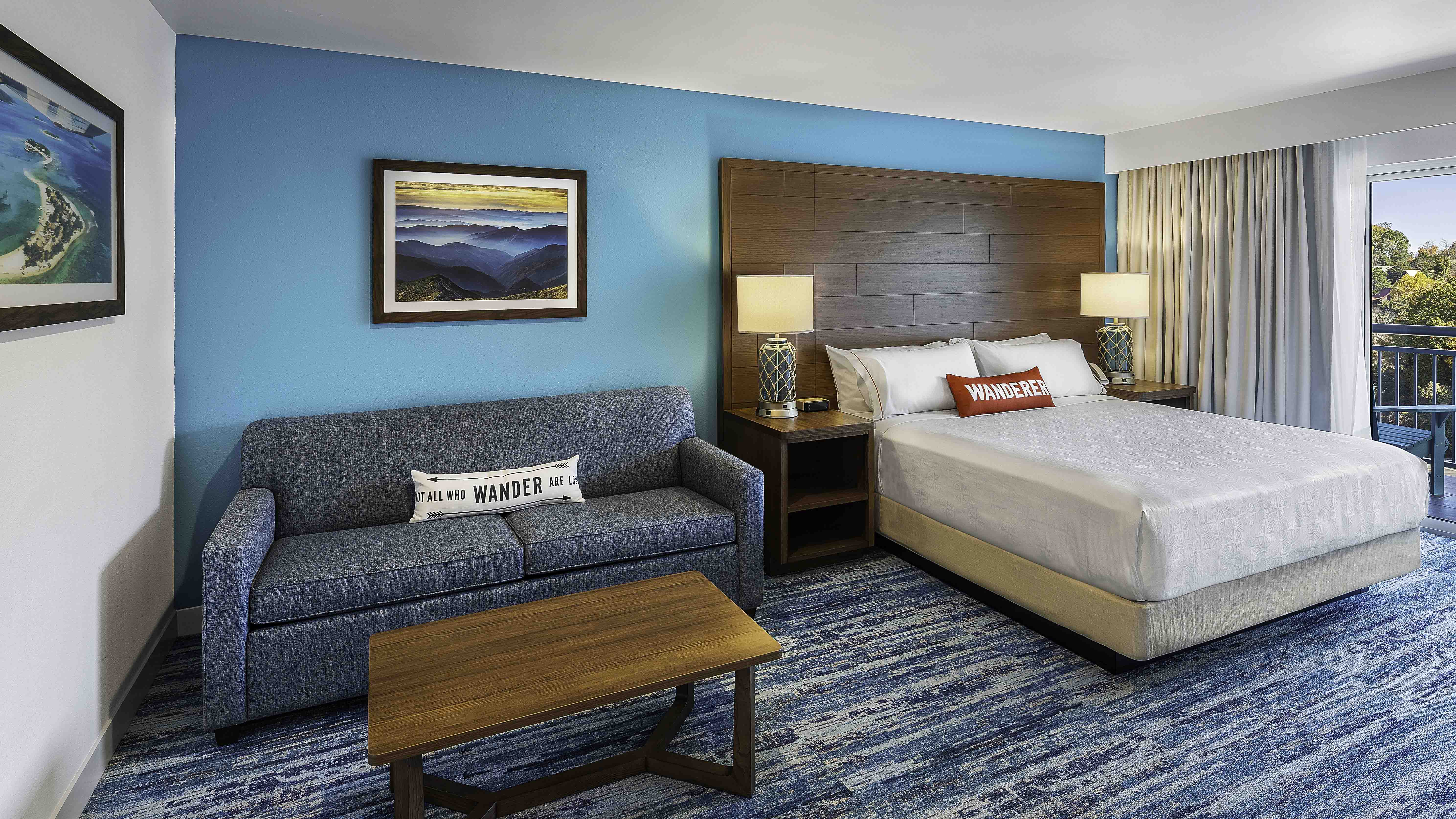 Hotel room with bed, sofa, and balcony, featuring turquoise accent wall and mountain artwork