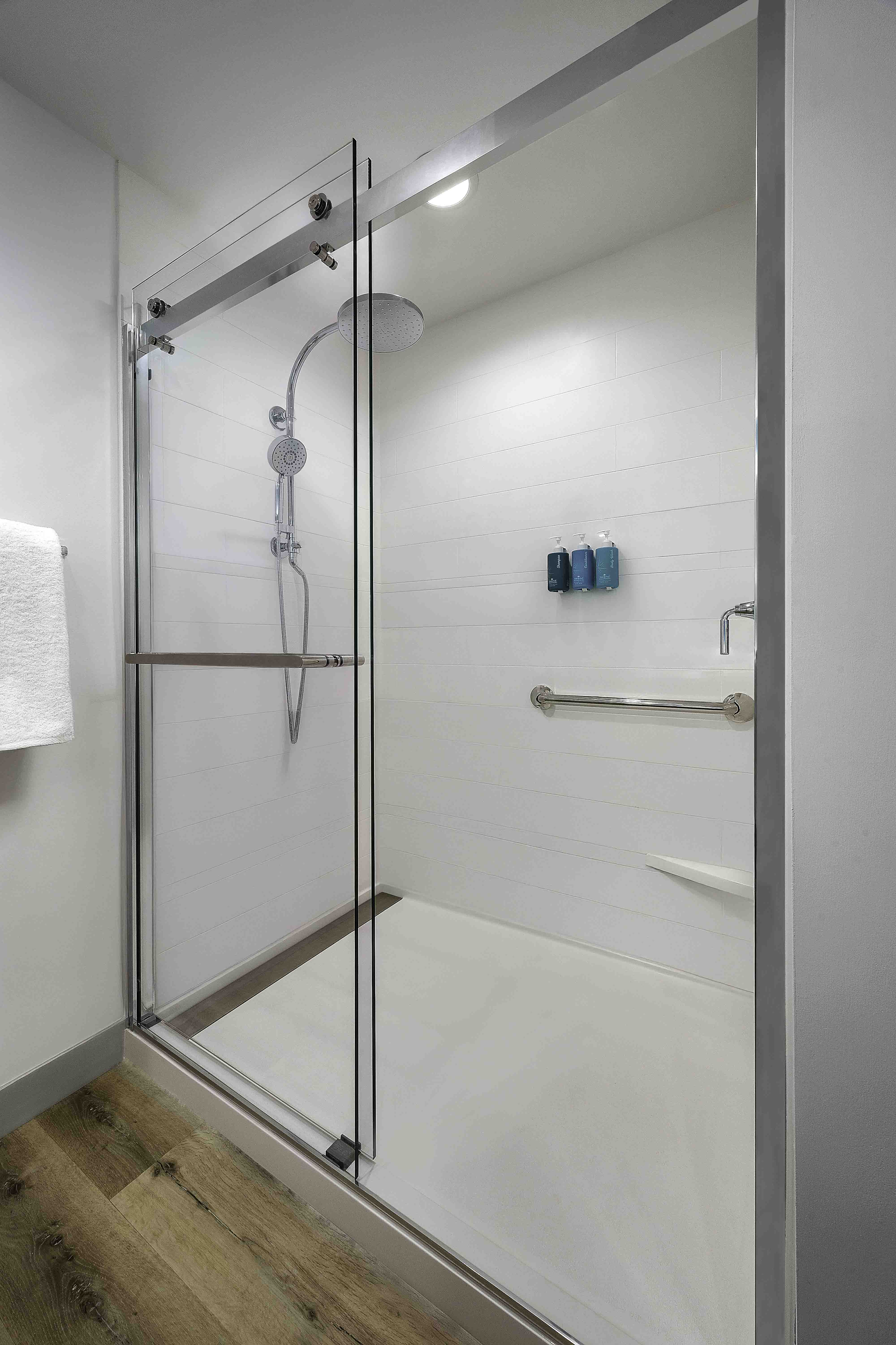 Glass walk-in shower with chrome fixtures and grab bar in a modern bathroom by D&S Builders