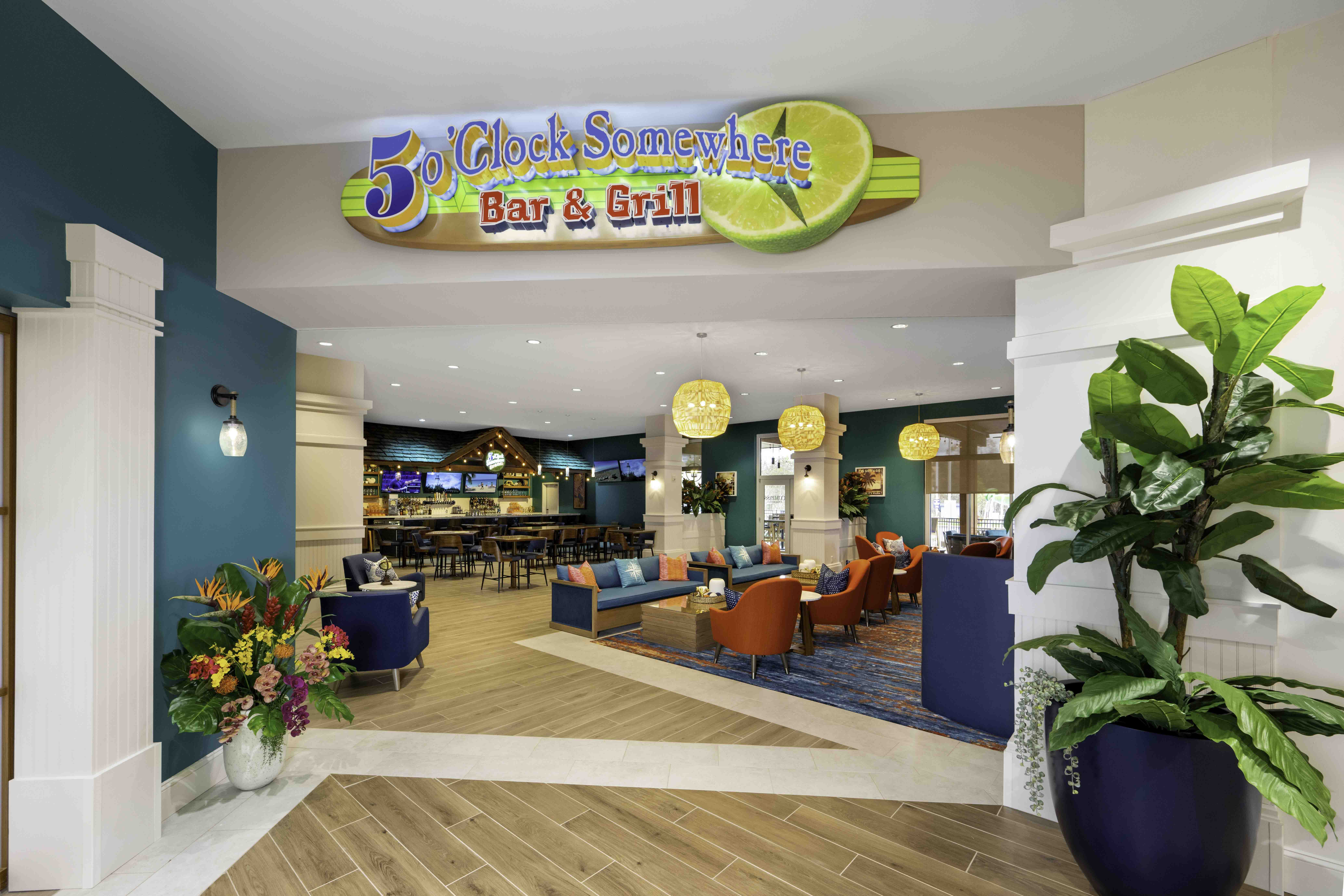 Colorful hospitality lobby with lounge seating and a bar under a 5 O’Clock Somewhere Bar & Grill sign