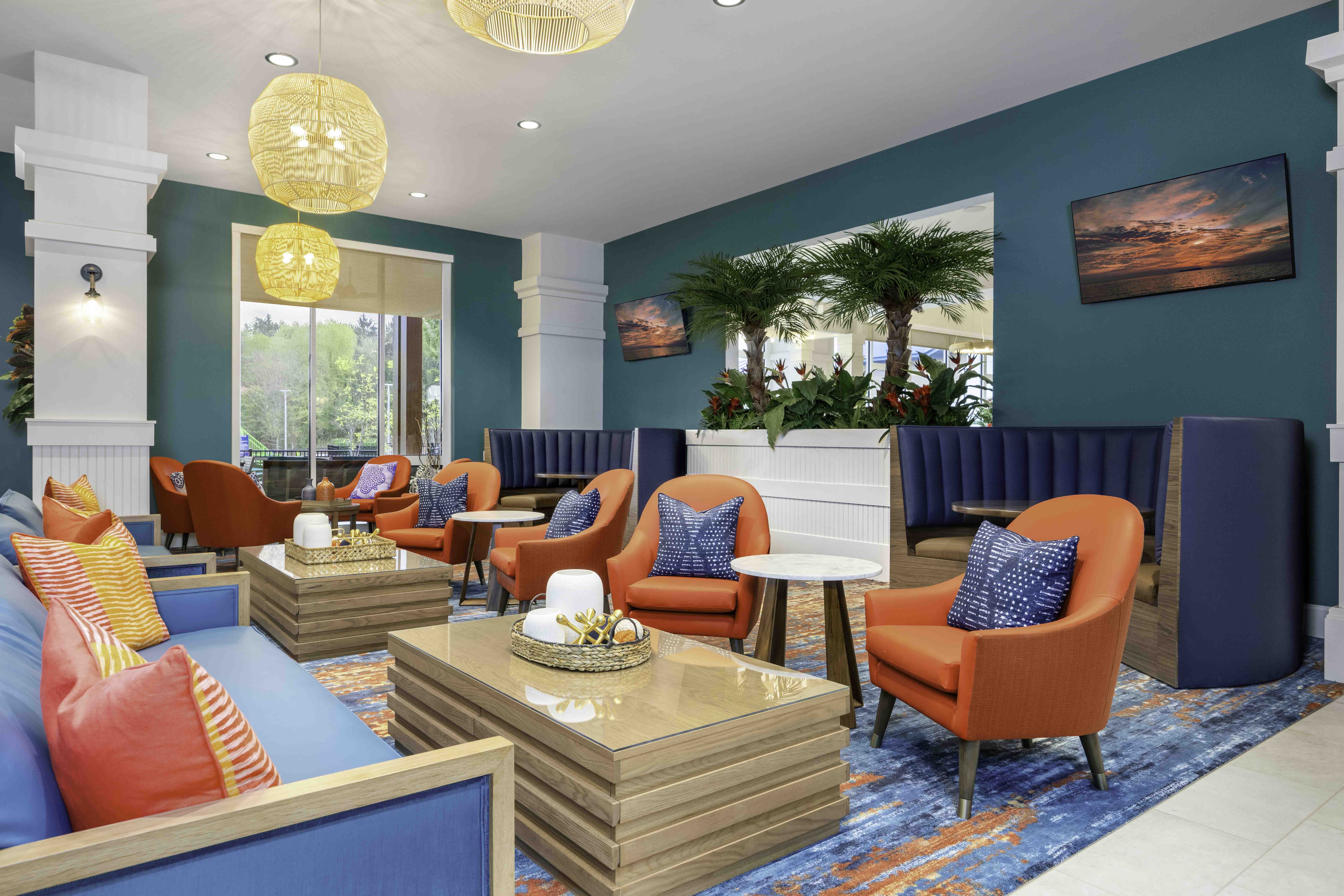 Colorful hospitality lounge with teal walls, orange chairs, blue booths, and tropical decor