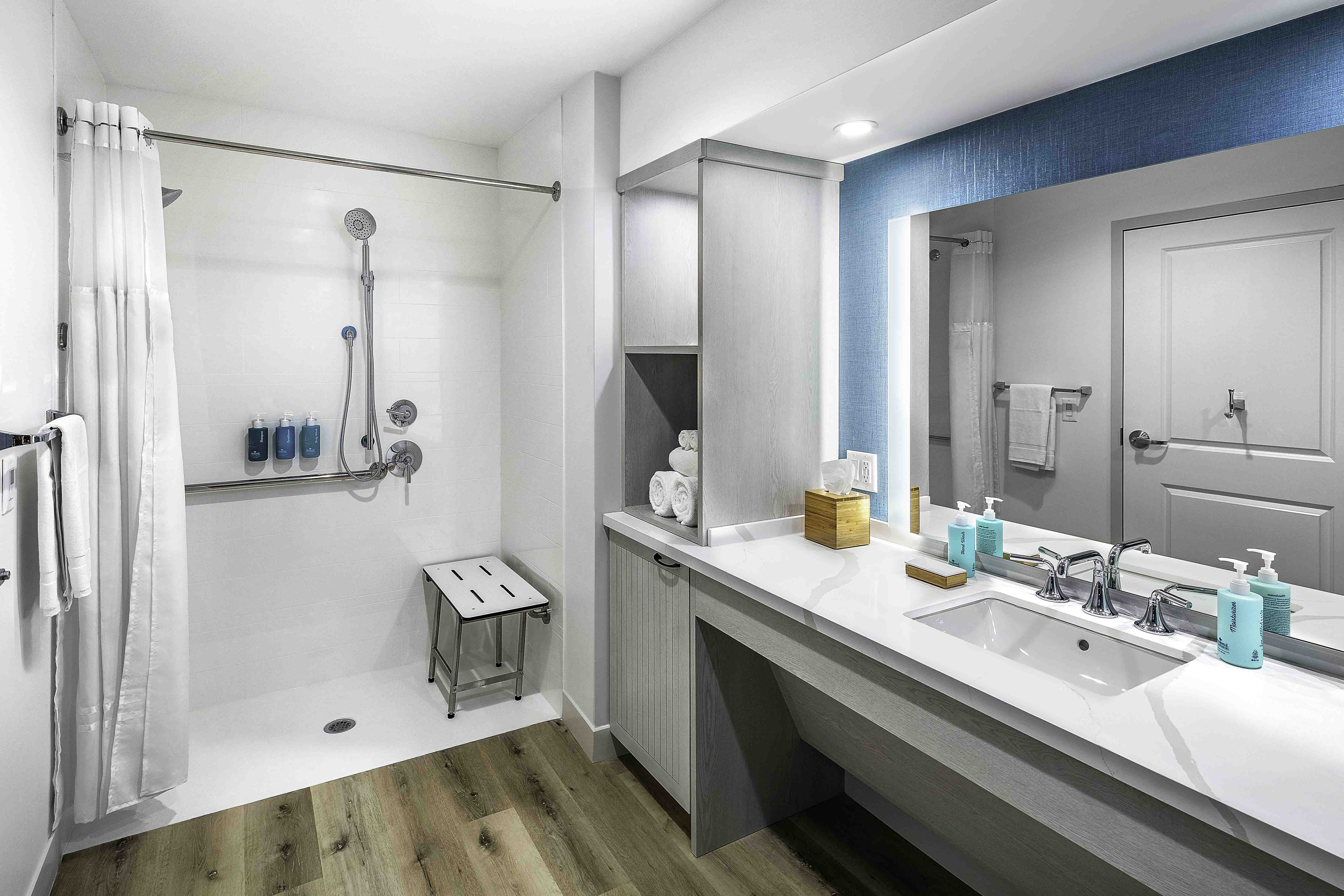Modern bathroom with walk-in shower, vanity, and blue accent wall by D&S Builders
