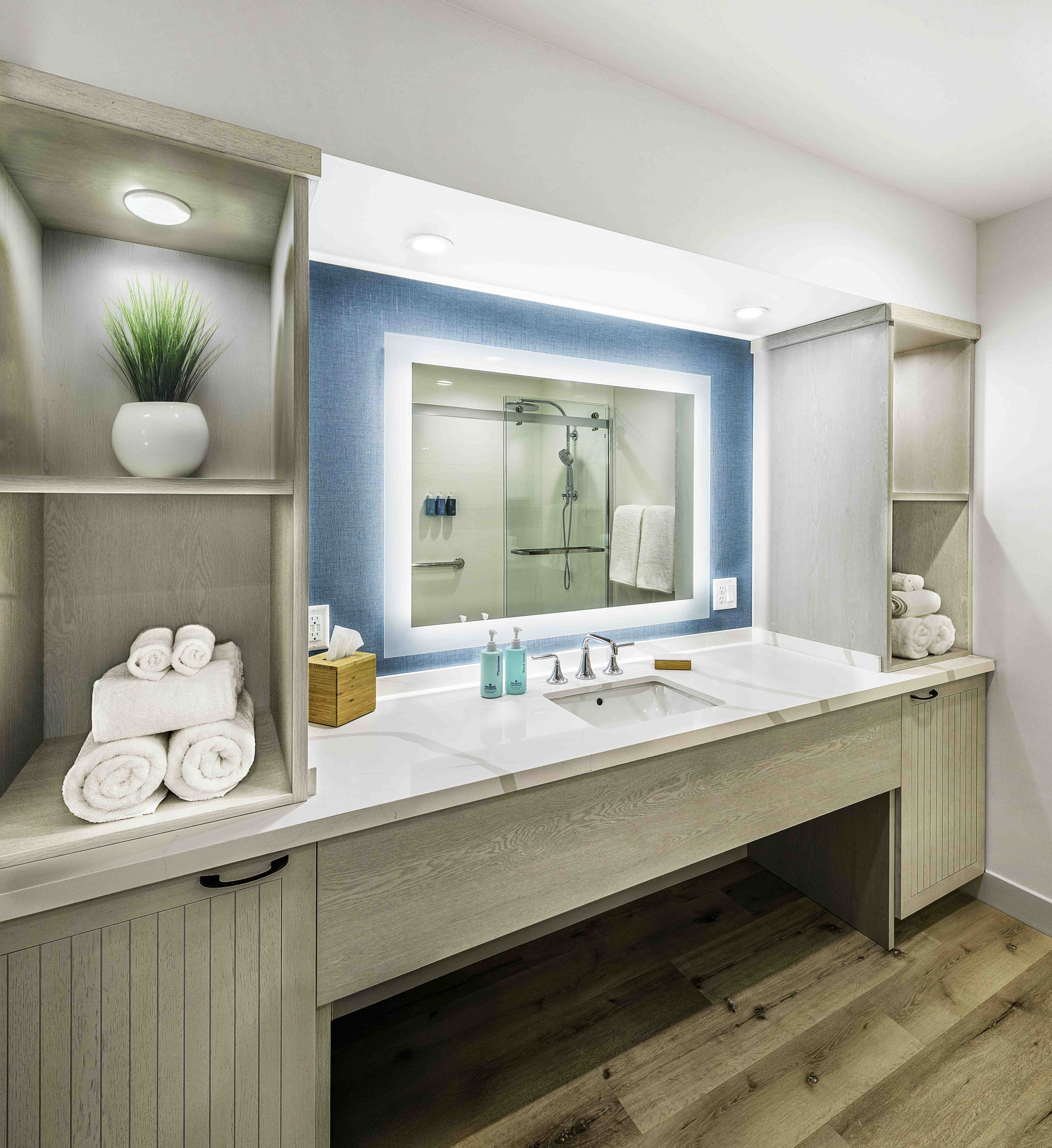 Modern bathroom vanity with lit mirror, open shelving, and folded towels