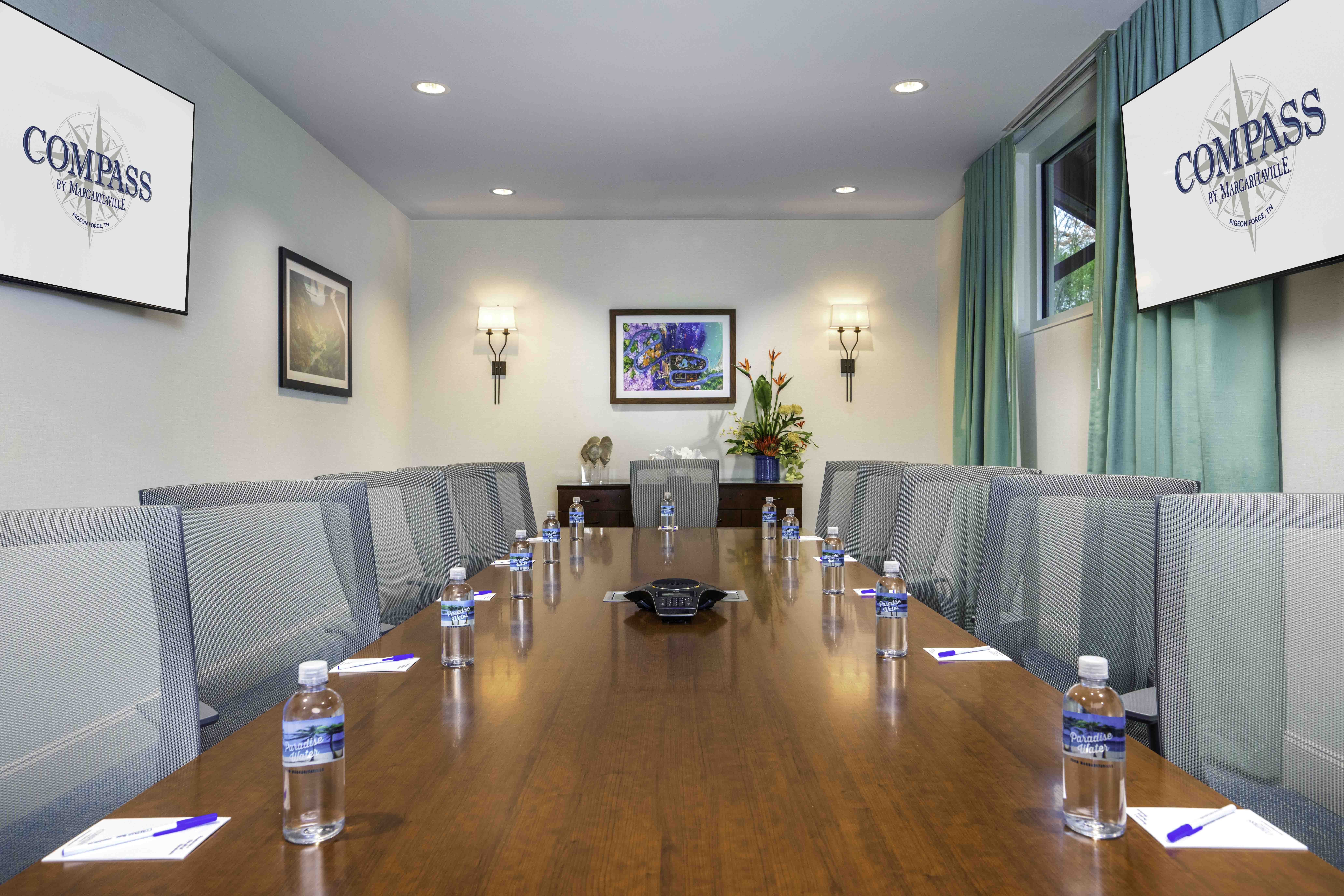 Conference room with long table, chairs, wall screens, and teal curtains in a hospitality setting