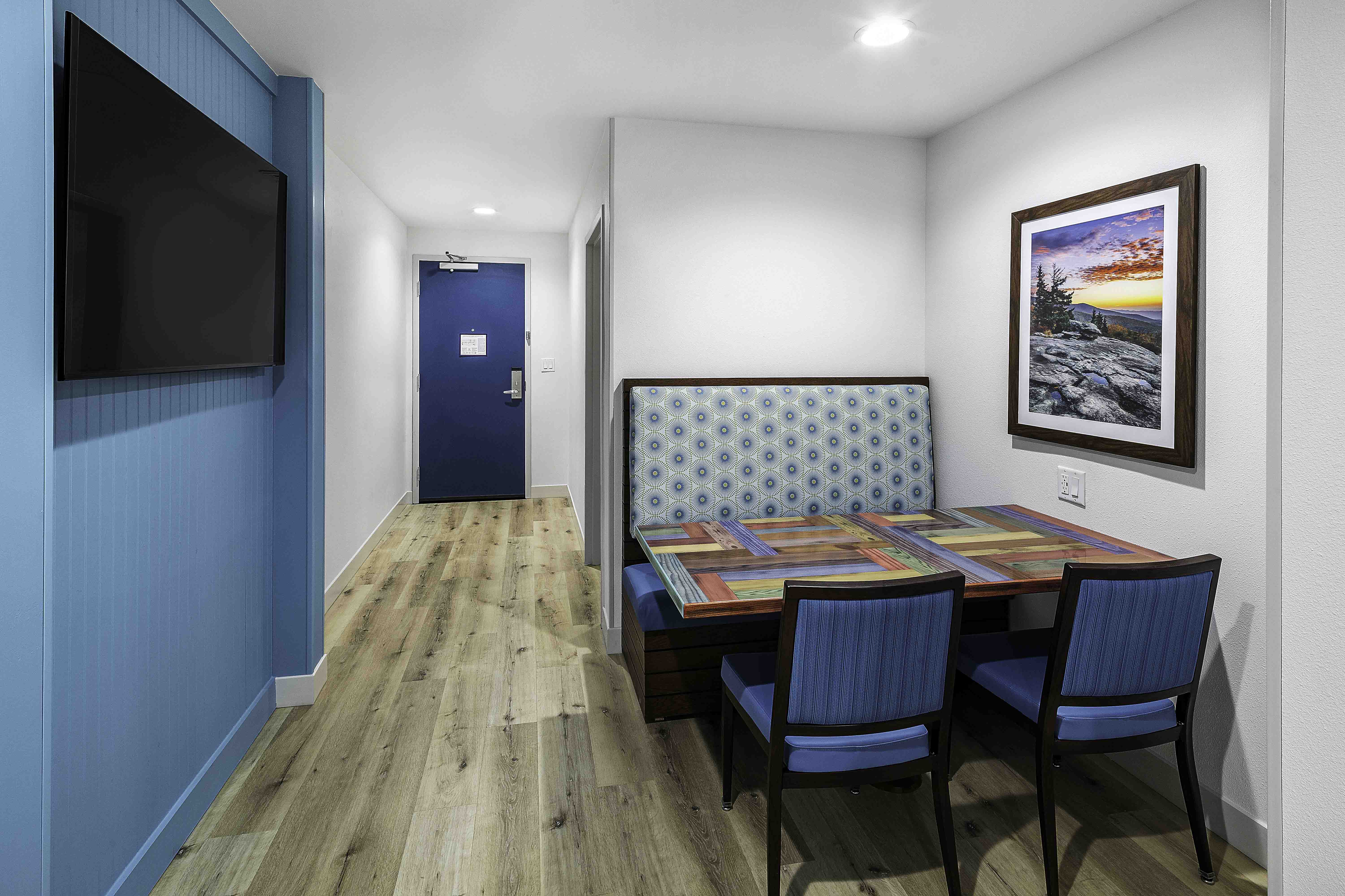Compact hospitality room with booth seating, wall-mounted TV, and blue door in a D&S Builders interior.
