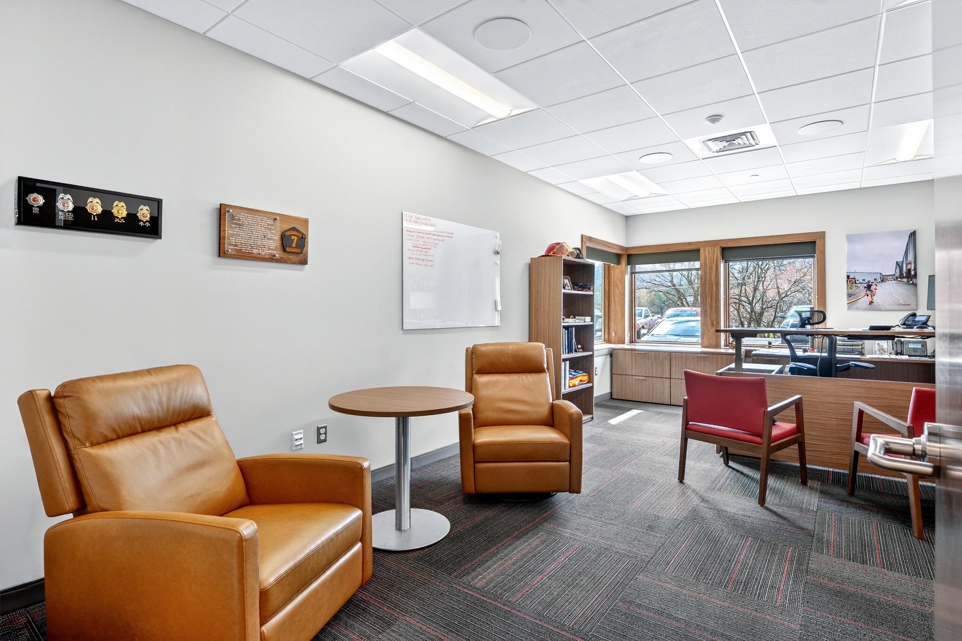 Modern office lounge with leather chairs, table, whiteboard, and desks at D&S Builders