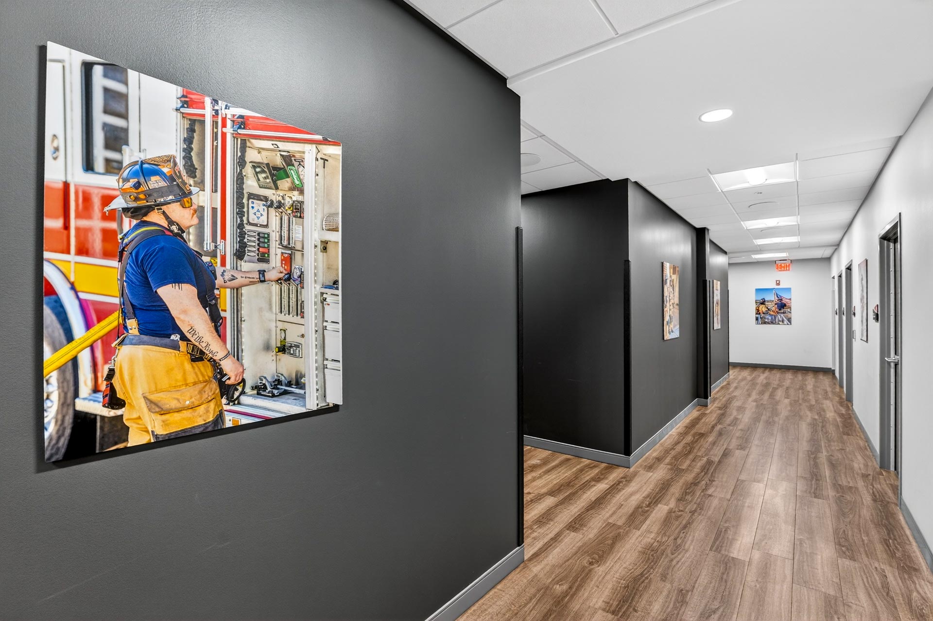 Hallway with framed fire truck photos and wood-look flooring in a D&S Builders office.