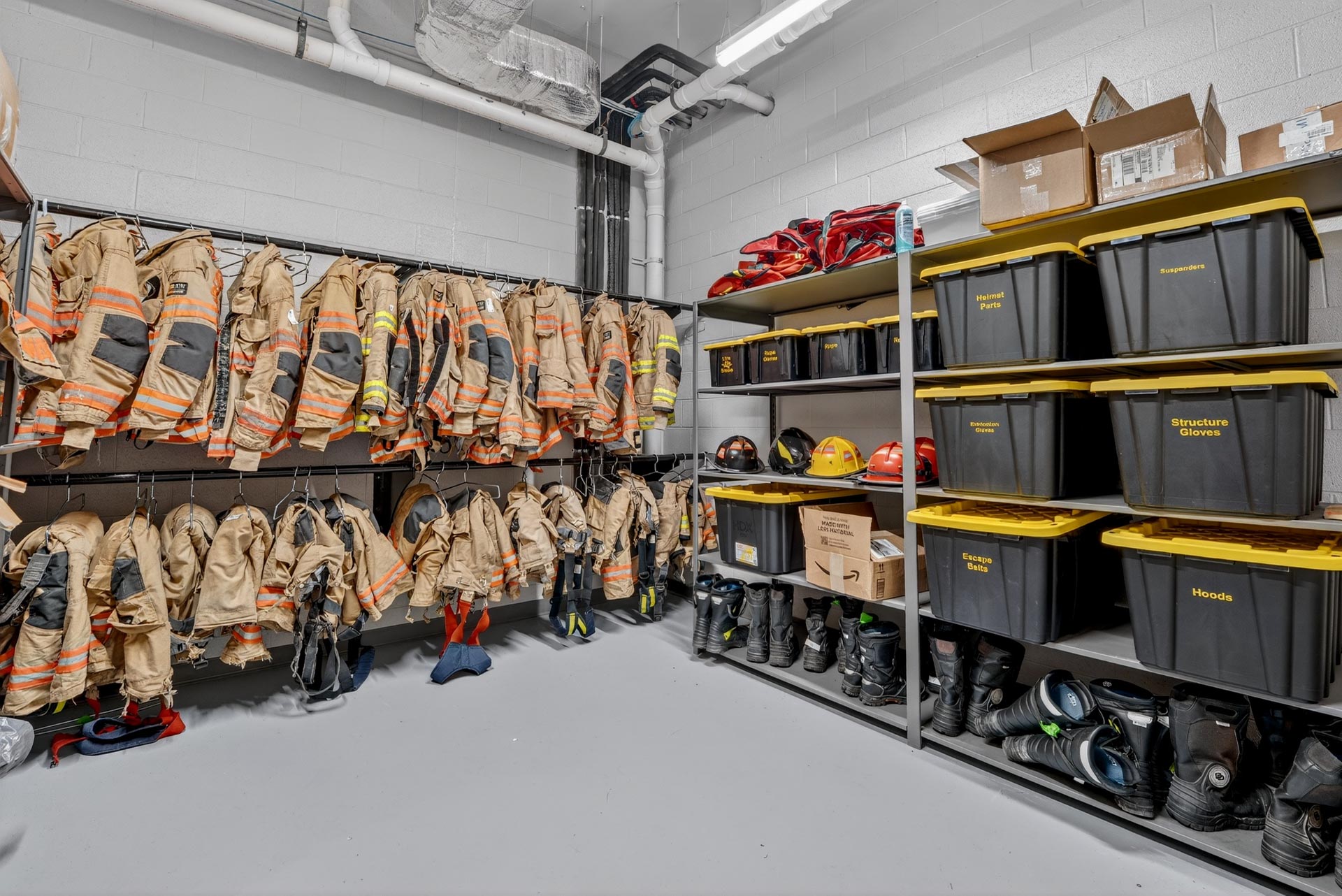 D&S Builders gear room with hanging firefighter coats, helmets, boots, and labeled storage bins