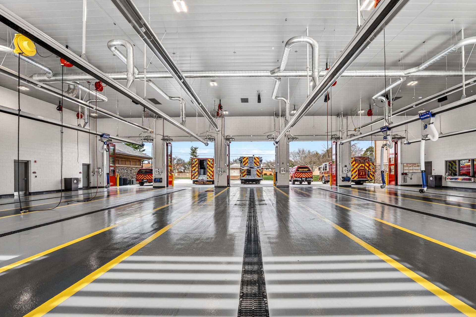 Modern fire station apparatus bay with fire trucks parked inside and open garage doors