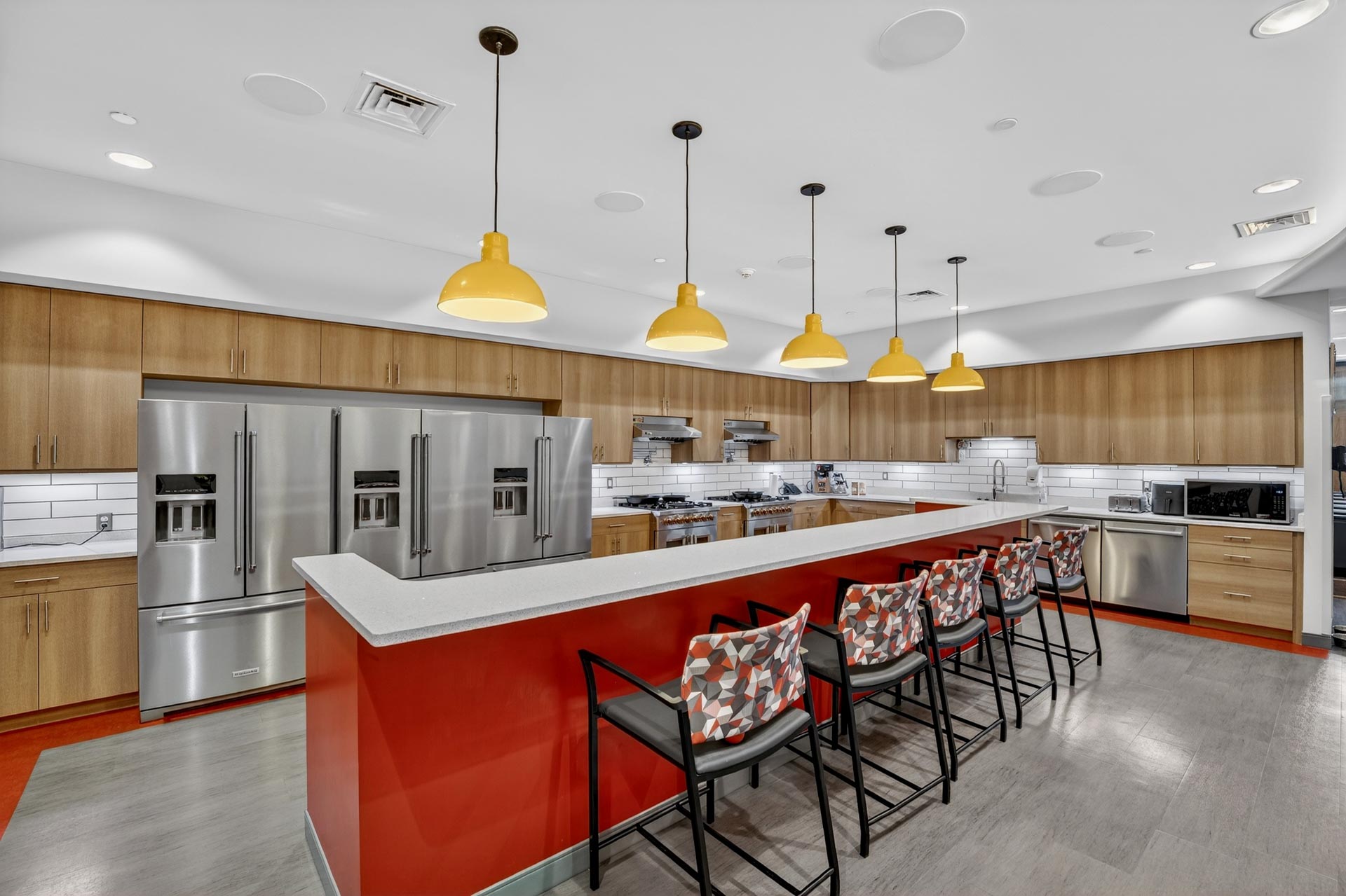 Modern commercial kitchen with red island, stainless appliances, and yellow pendant lights