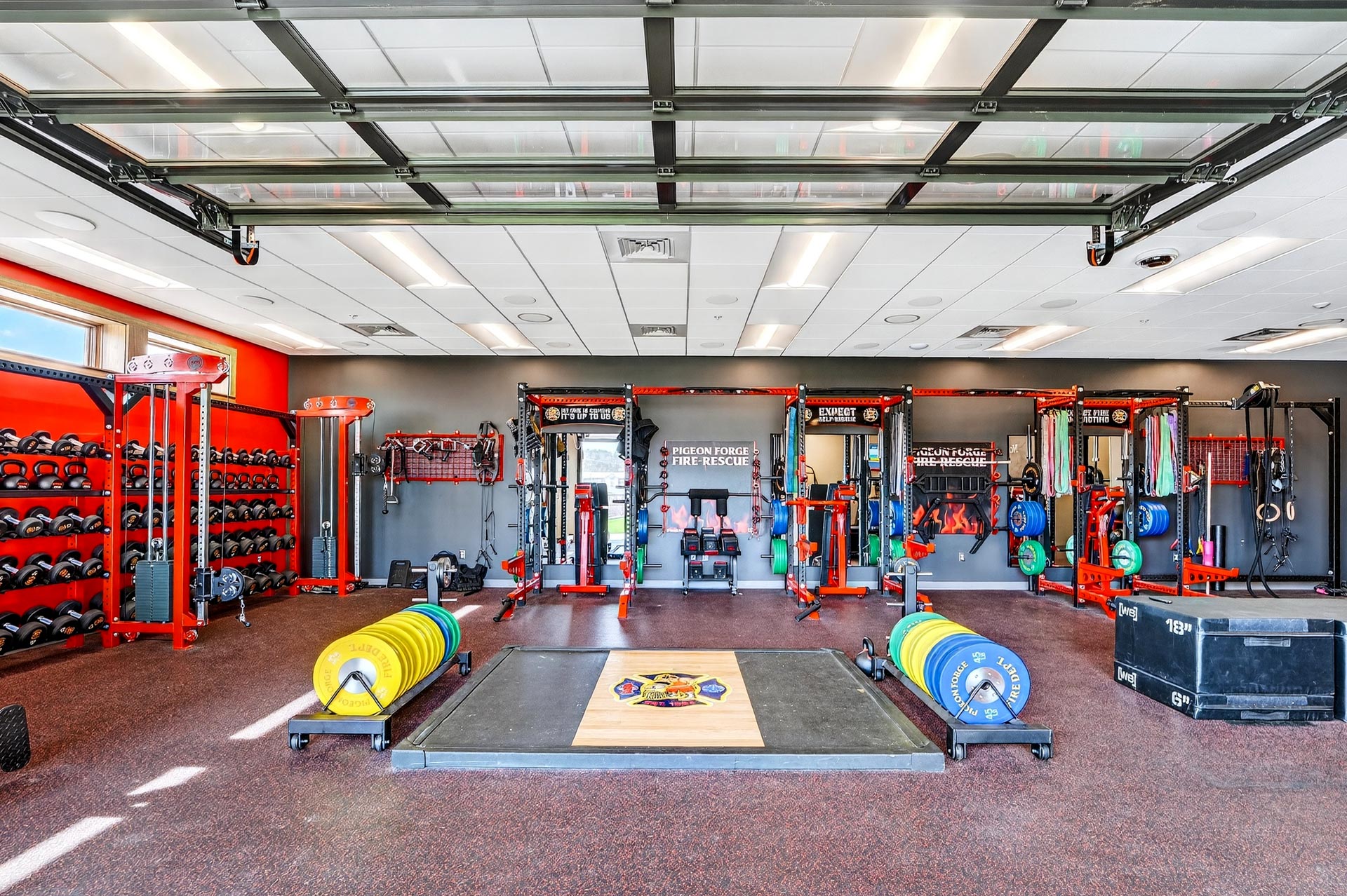 Fire station training gym with weight racks, lifting platforms, and overhead garage doors