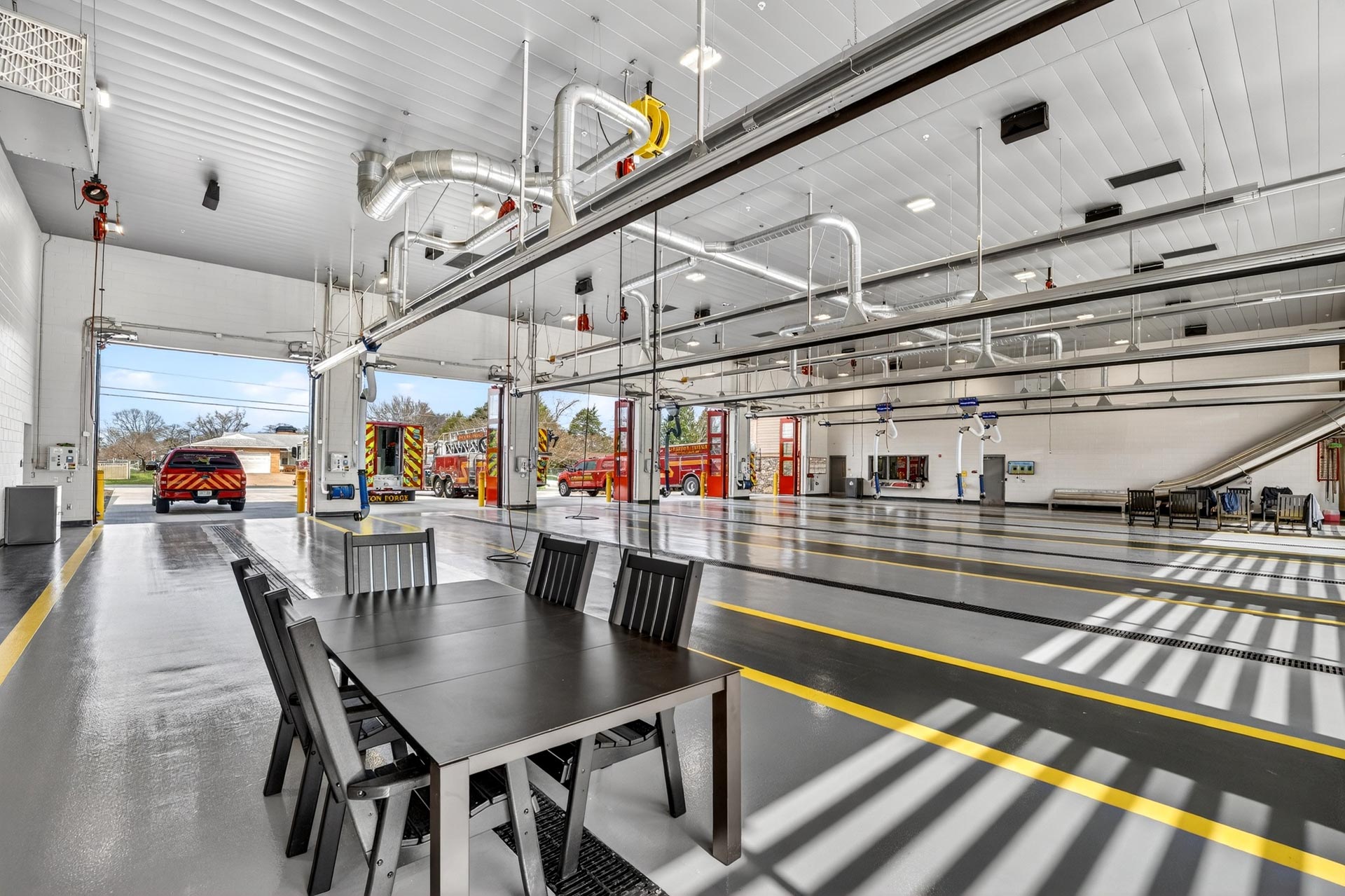 Fire station apparatus bay with trucks, overhead ventilation, and a table in the foreground