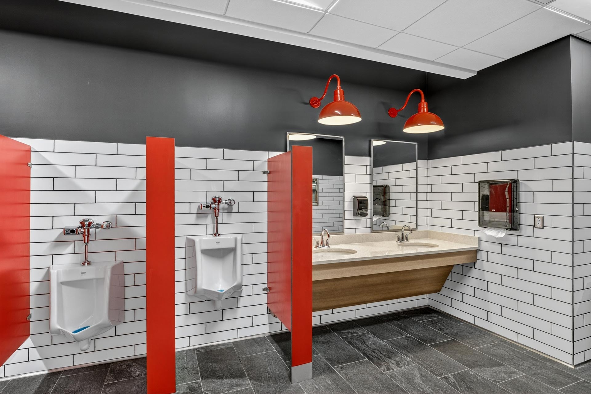 Modern commercial restroom with red stall dividers, white tile walls, and double sinks by D&S Builders