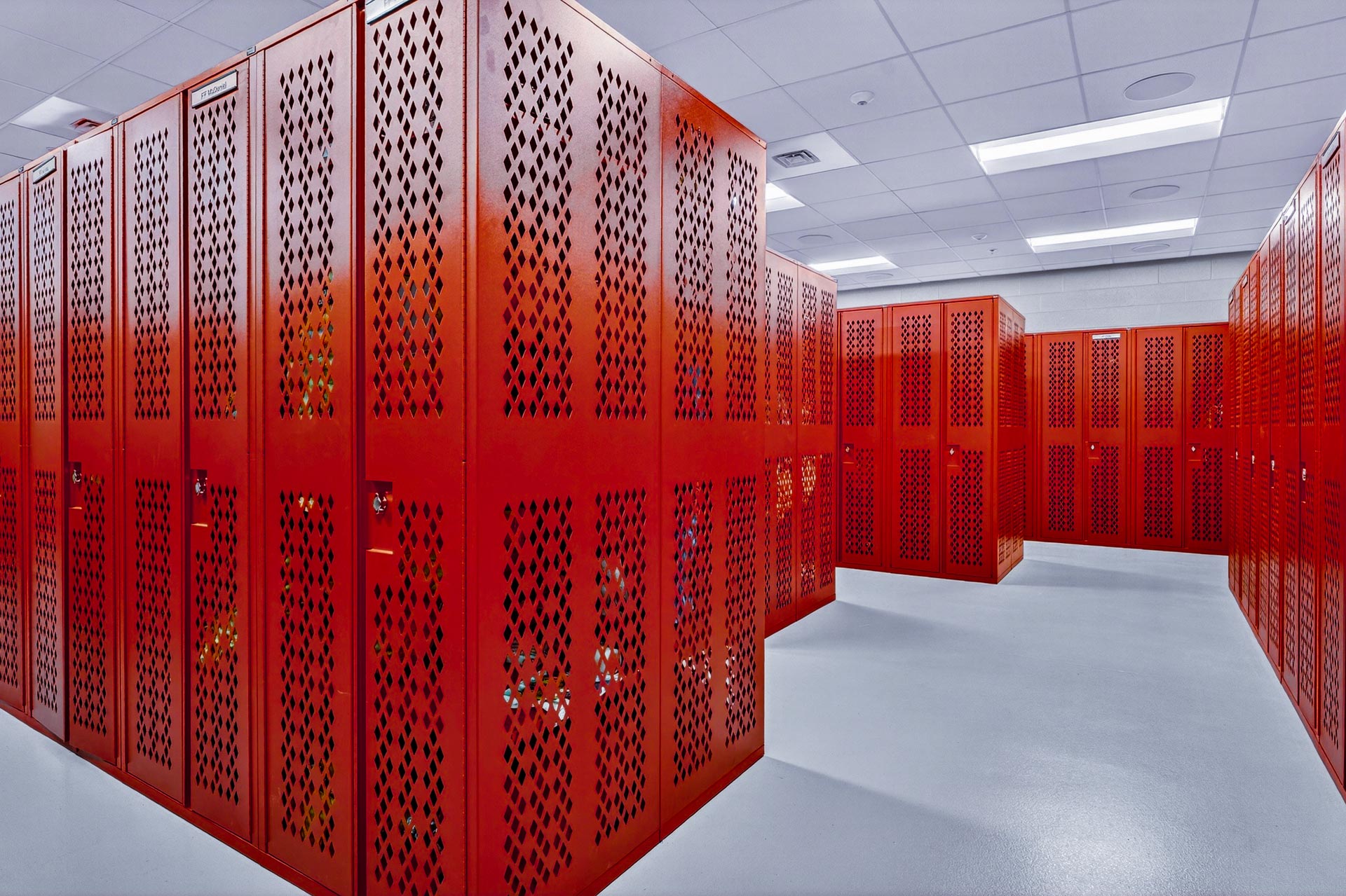 Bright locker room with rows of red metal lockers and white ceiling panels