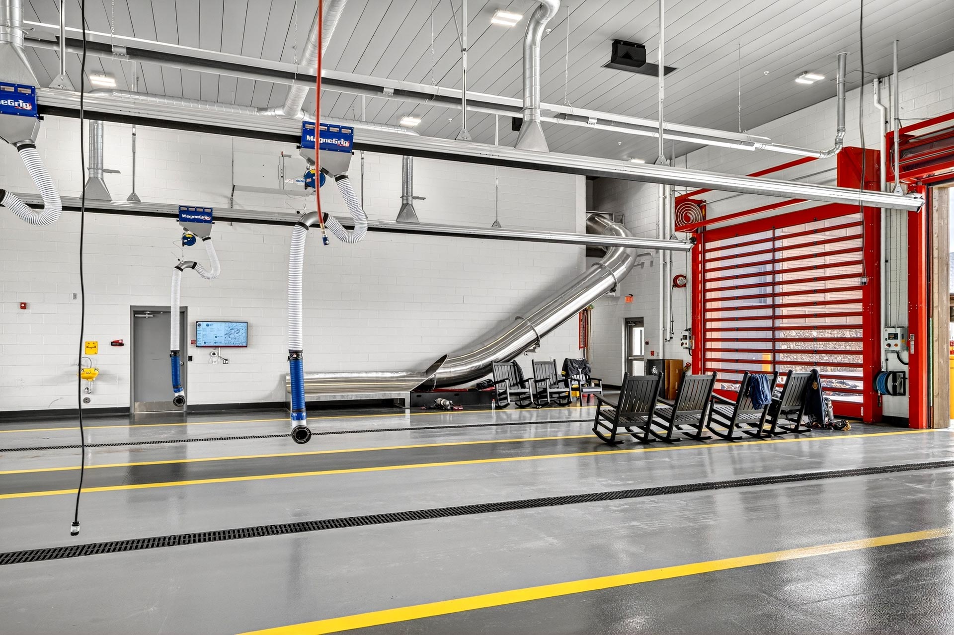 Modern fire station bay with overhead exhaust hoses, polished floor, and red equipment door