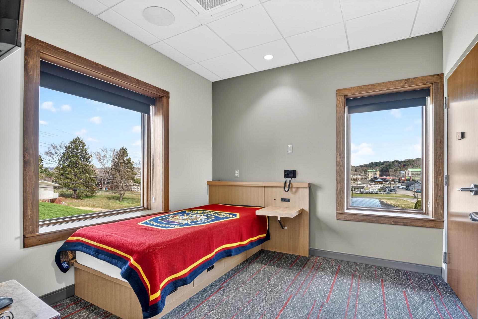 Hospital room with a single bed, large windows, and a view outside
