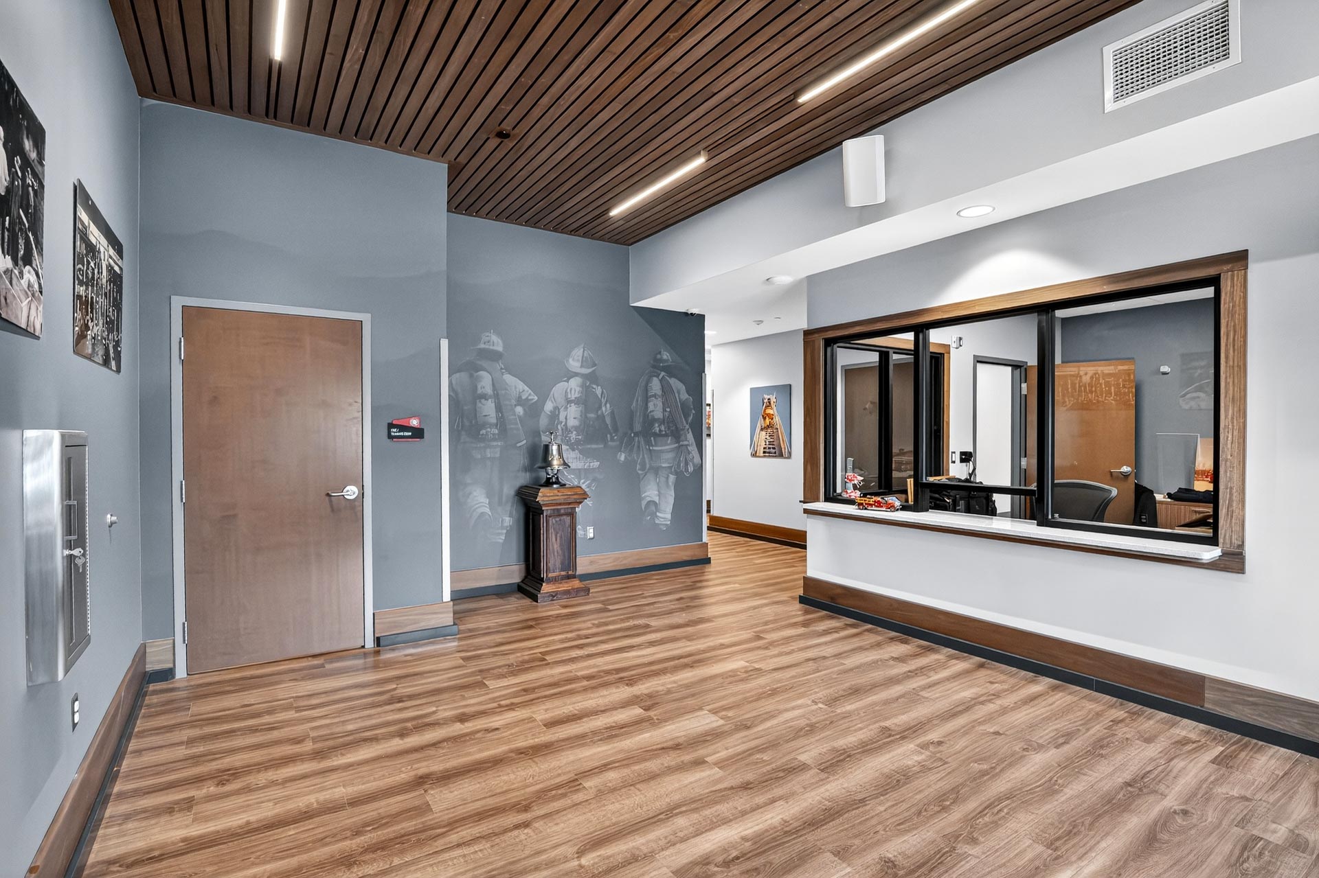 Modern hospitality lobby with wood floors, gray walls, and a reception window by D&S Builders