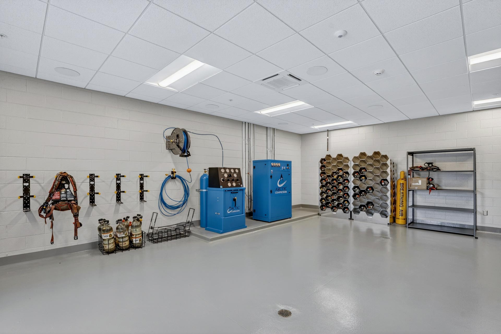 Industrial equipment room with wall-mounted gear, gas cylinders, and storage racks by D&S Builders