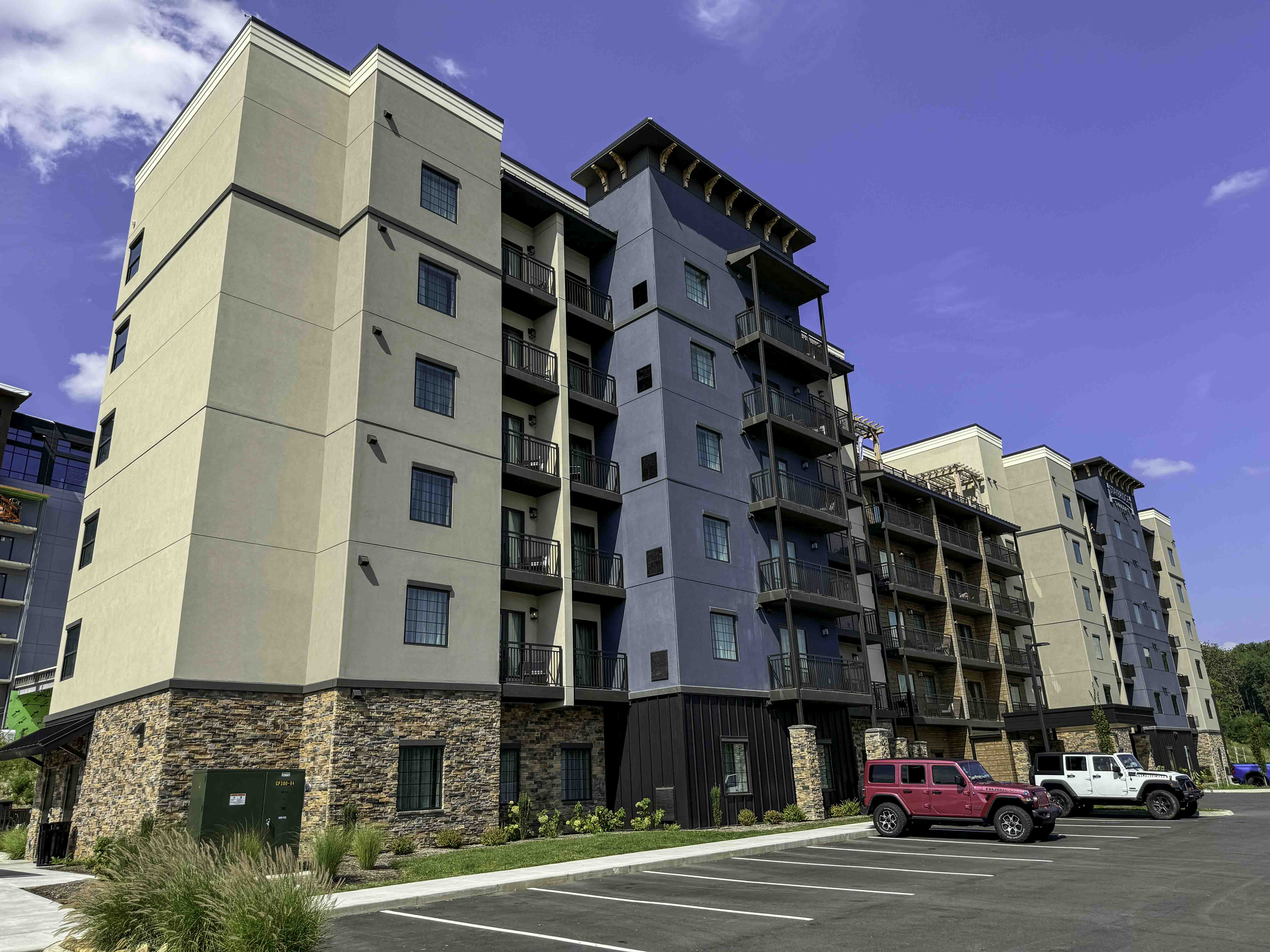Multi-story hospitality building with balconies and parked Jeeps under a blue sky