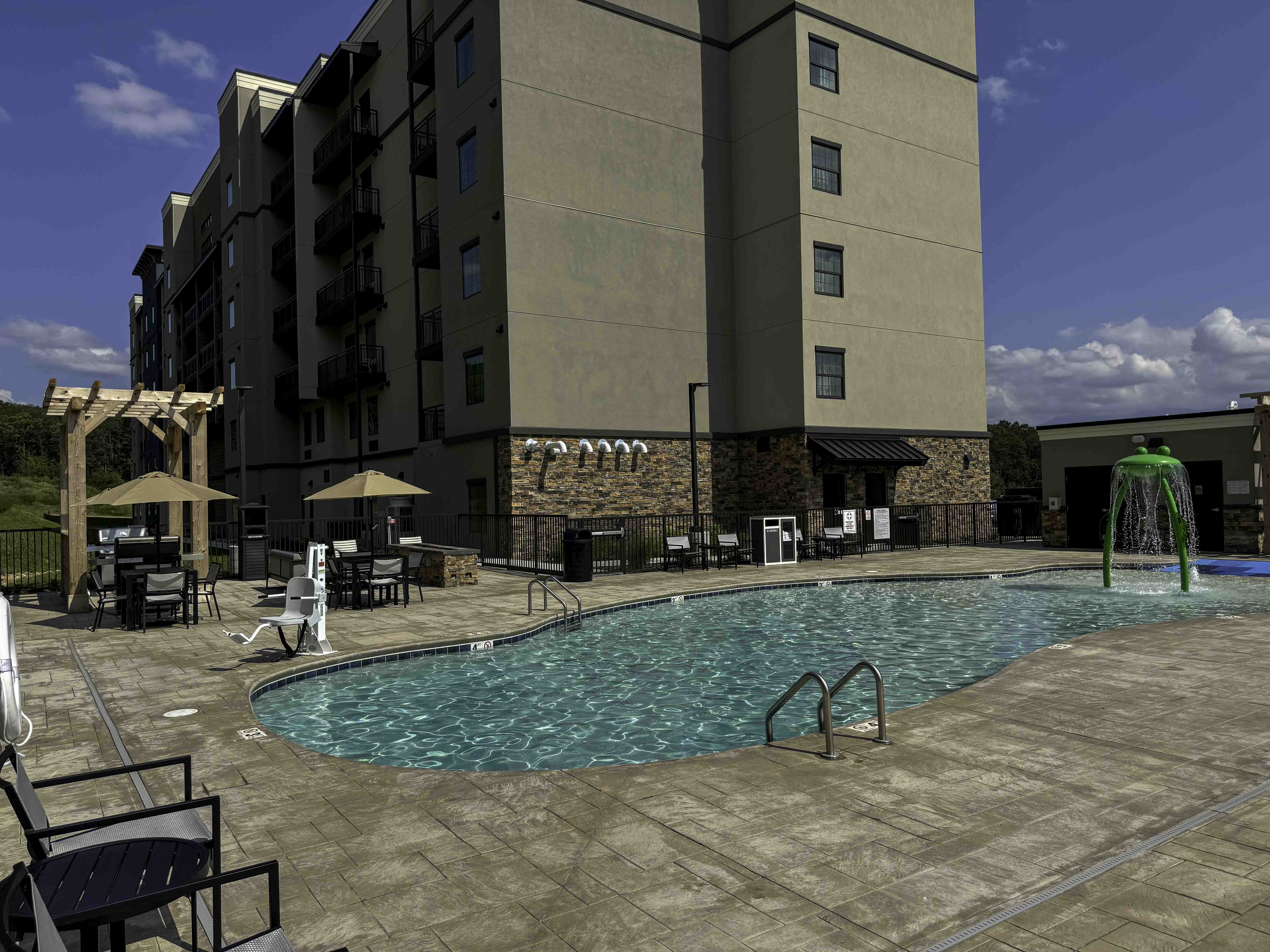 Hotel pool area beside a multi-story building, with patio seating and a water feature