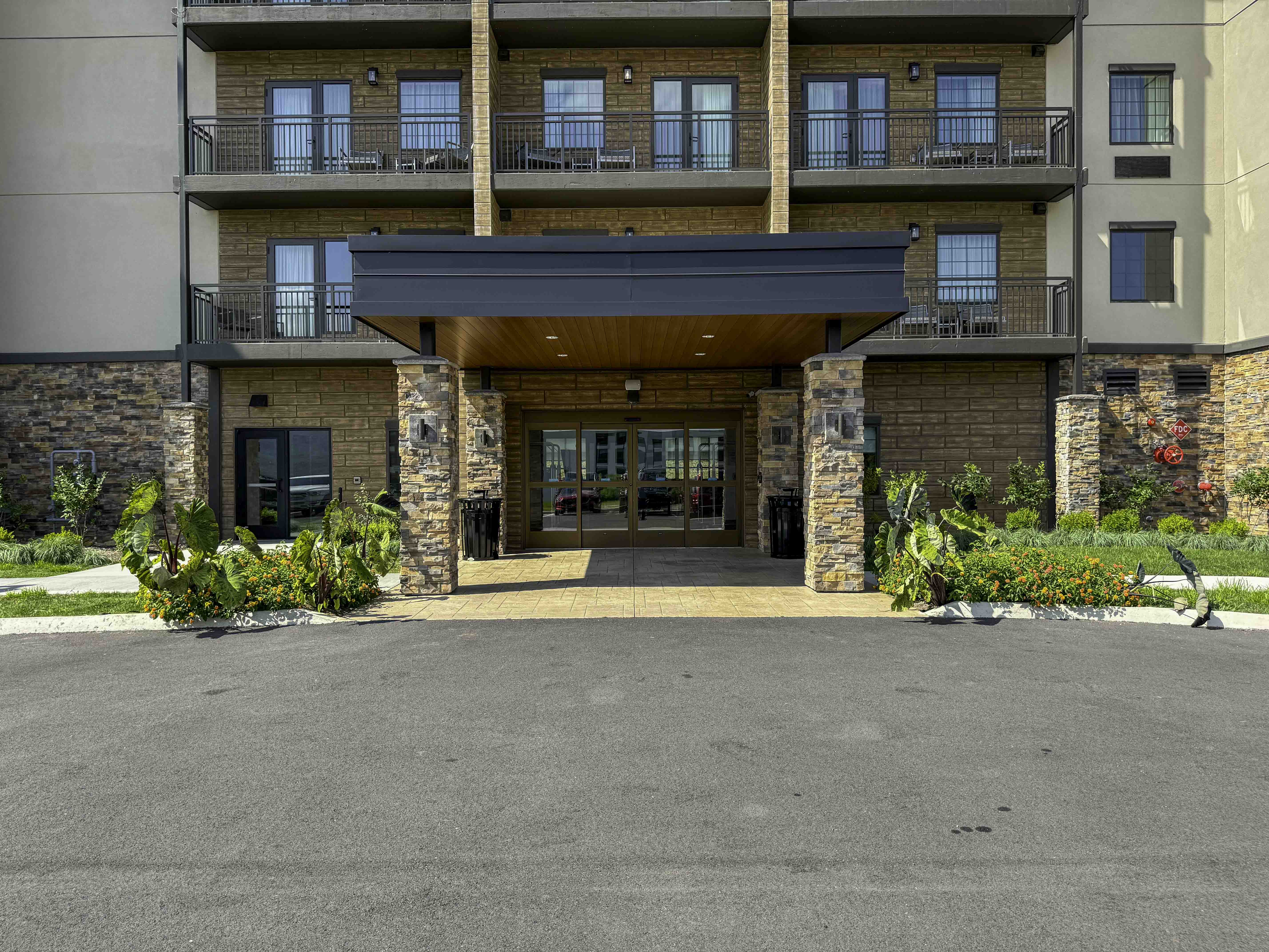 Modern hotel entrance with stone columns, balconies, and landscaped planters