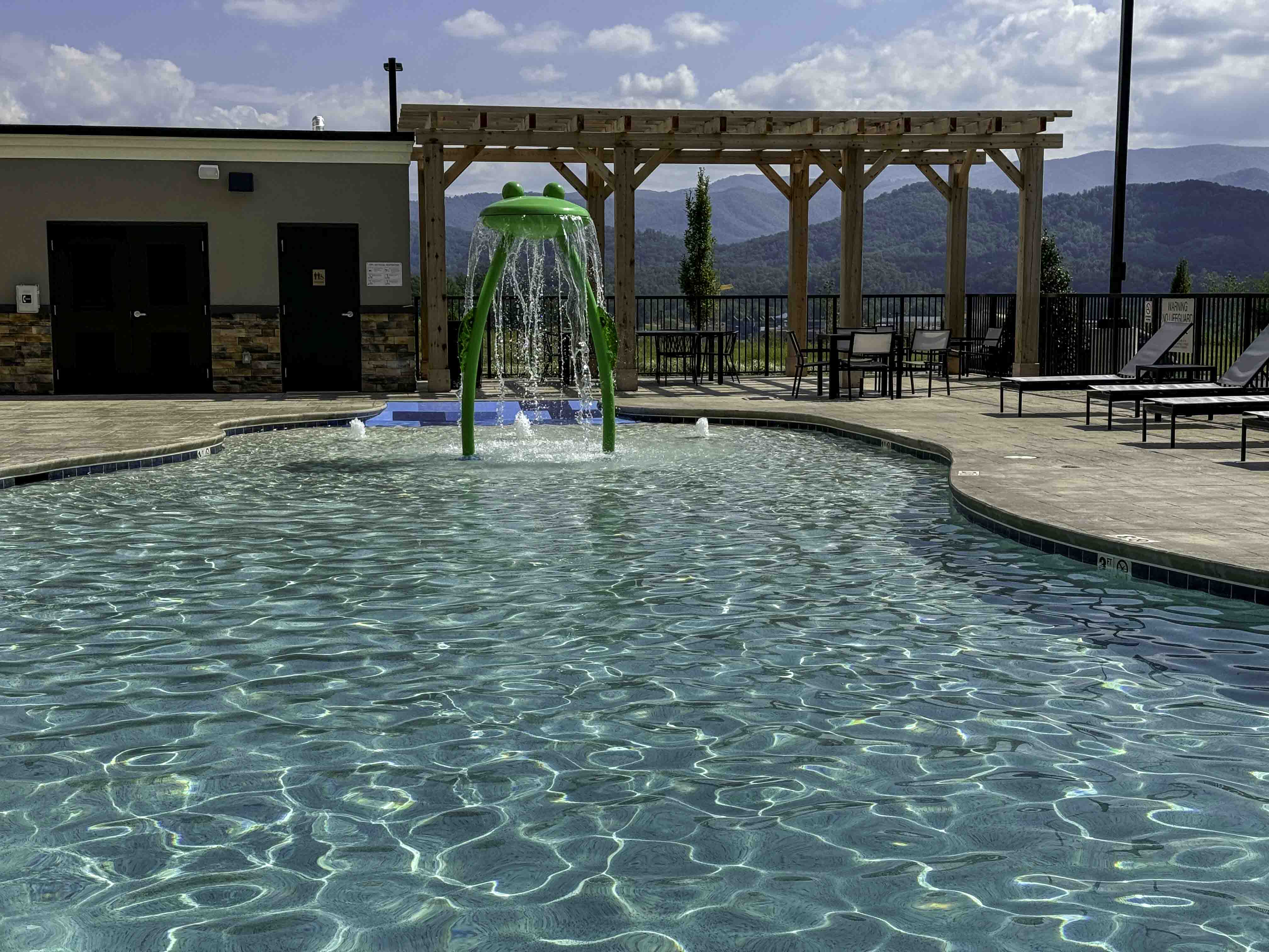 Outdoor pool with a green splash fountain, pergola seating, and mountain views at a D&S Builders project