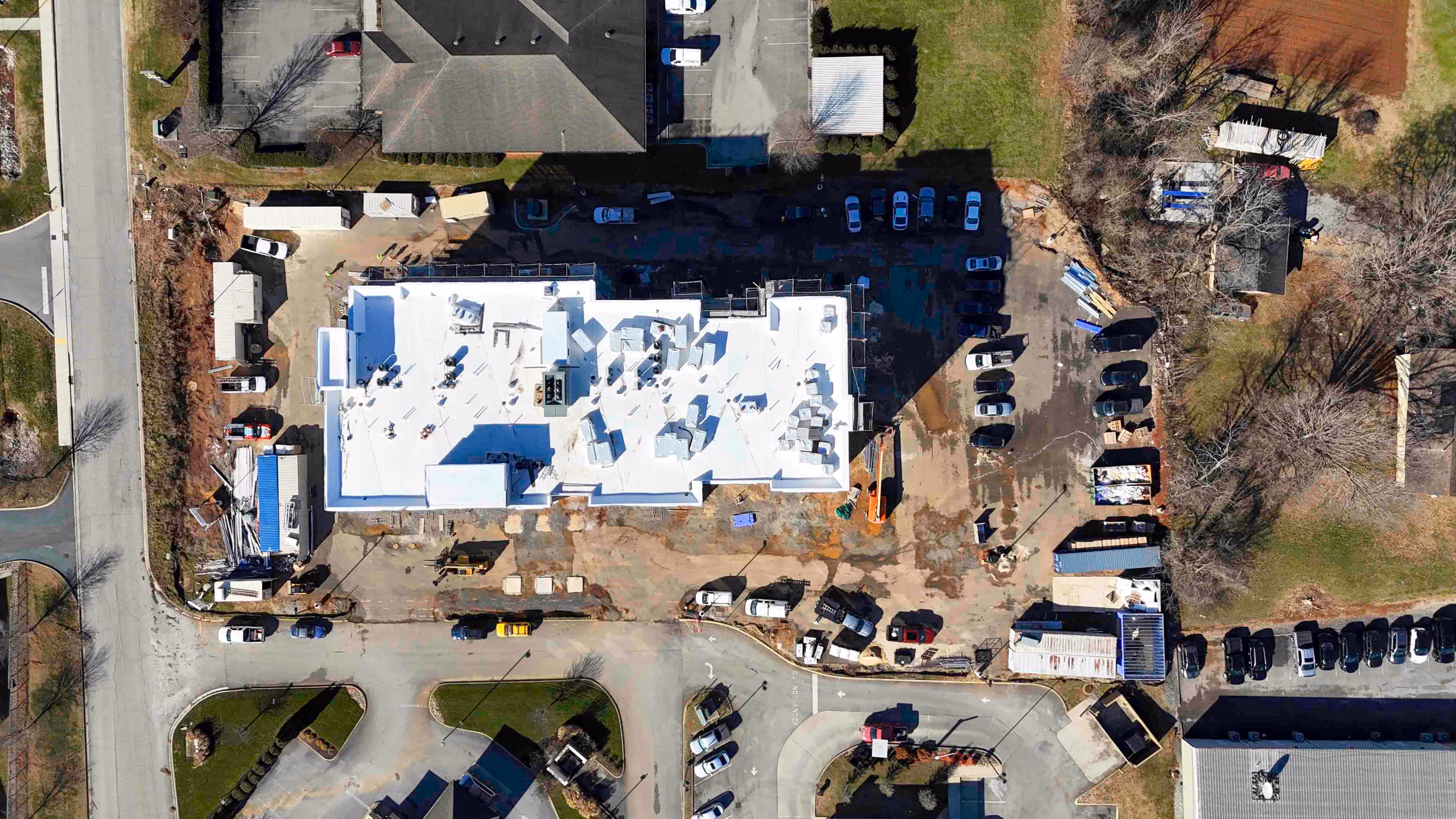 Aerial view of a large construction site with a white-roofed building and parked vehicles.