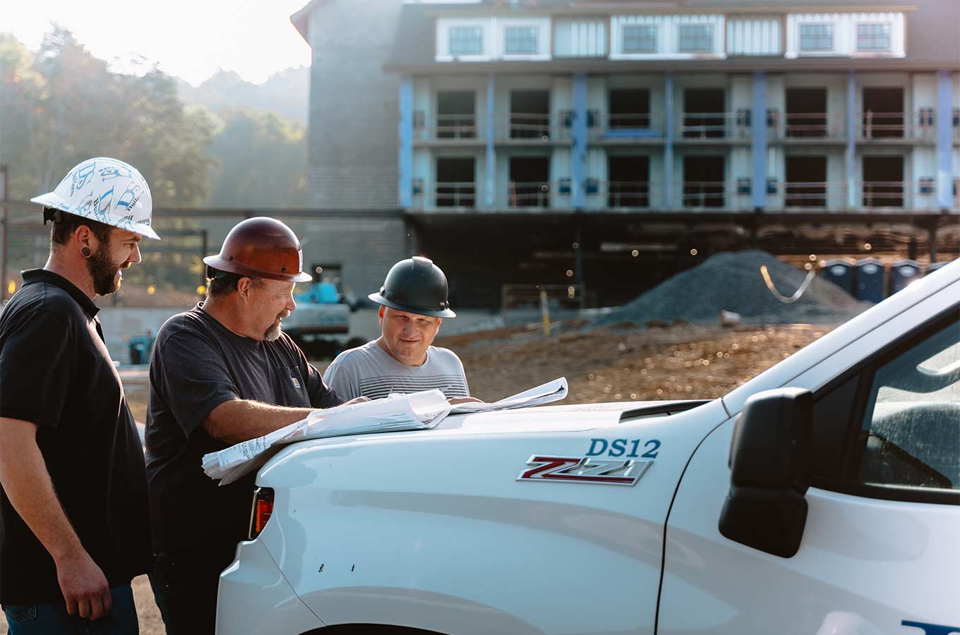 Construction workers reviewing plans beside a truck at a hospitality construction site